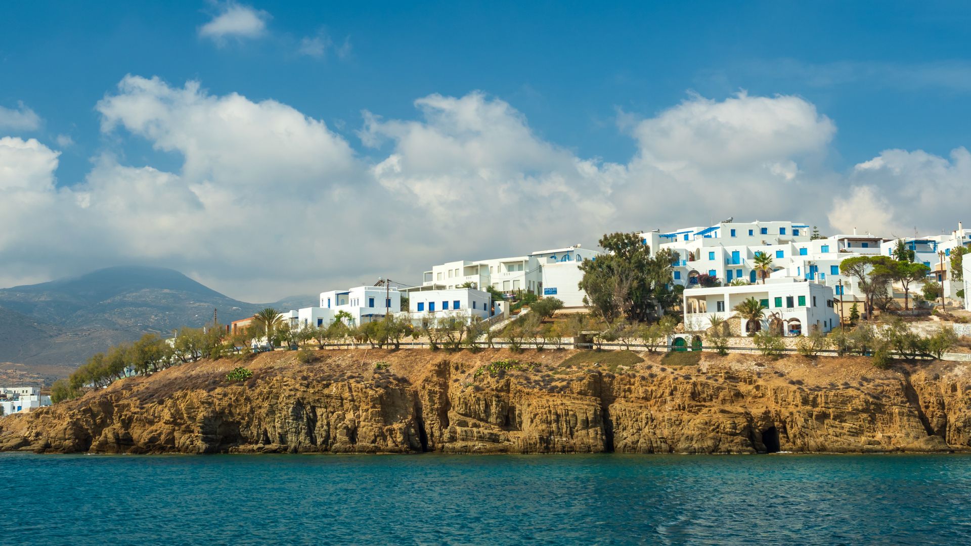 A coastal hillside village with white buildings and blue accents, overlooking a blue sea.