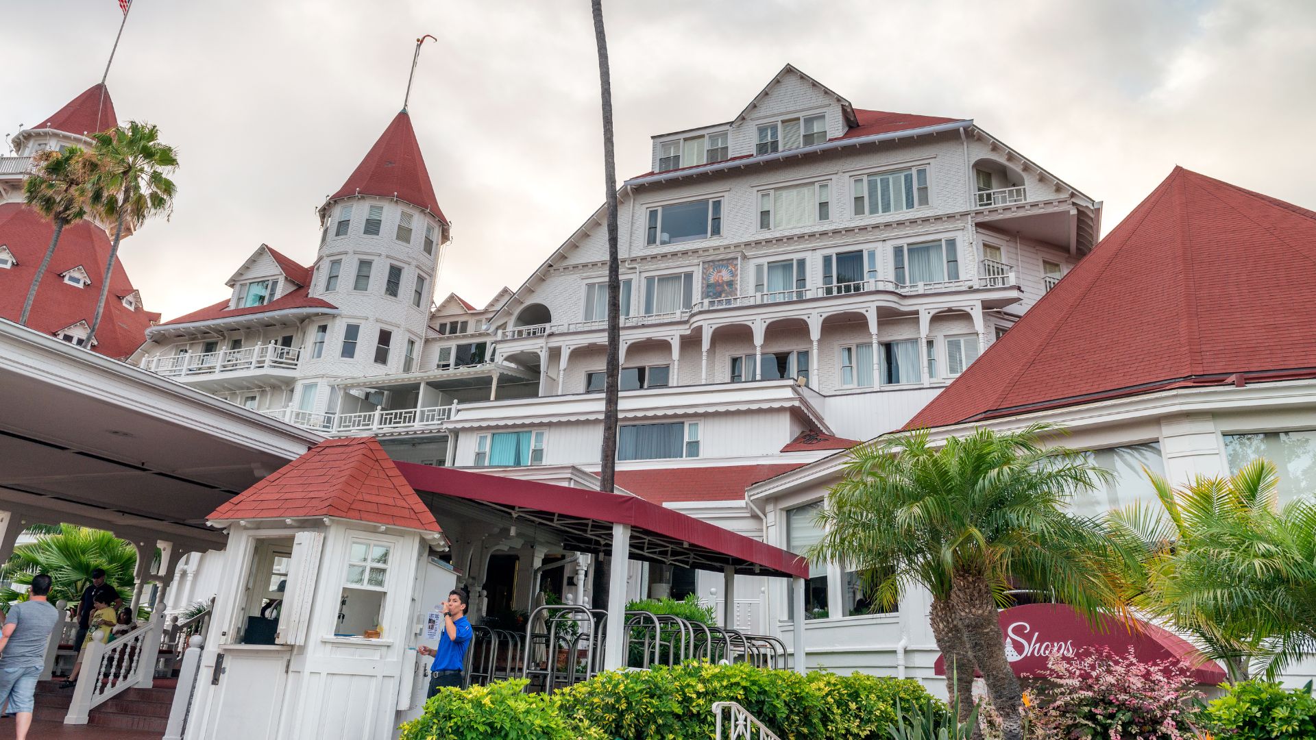 A large, historic white hotel with red-tiled roofs and prominent turrets, featuring Victorian architecture and surrounded by lush green landscaping and palm trees