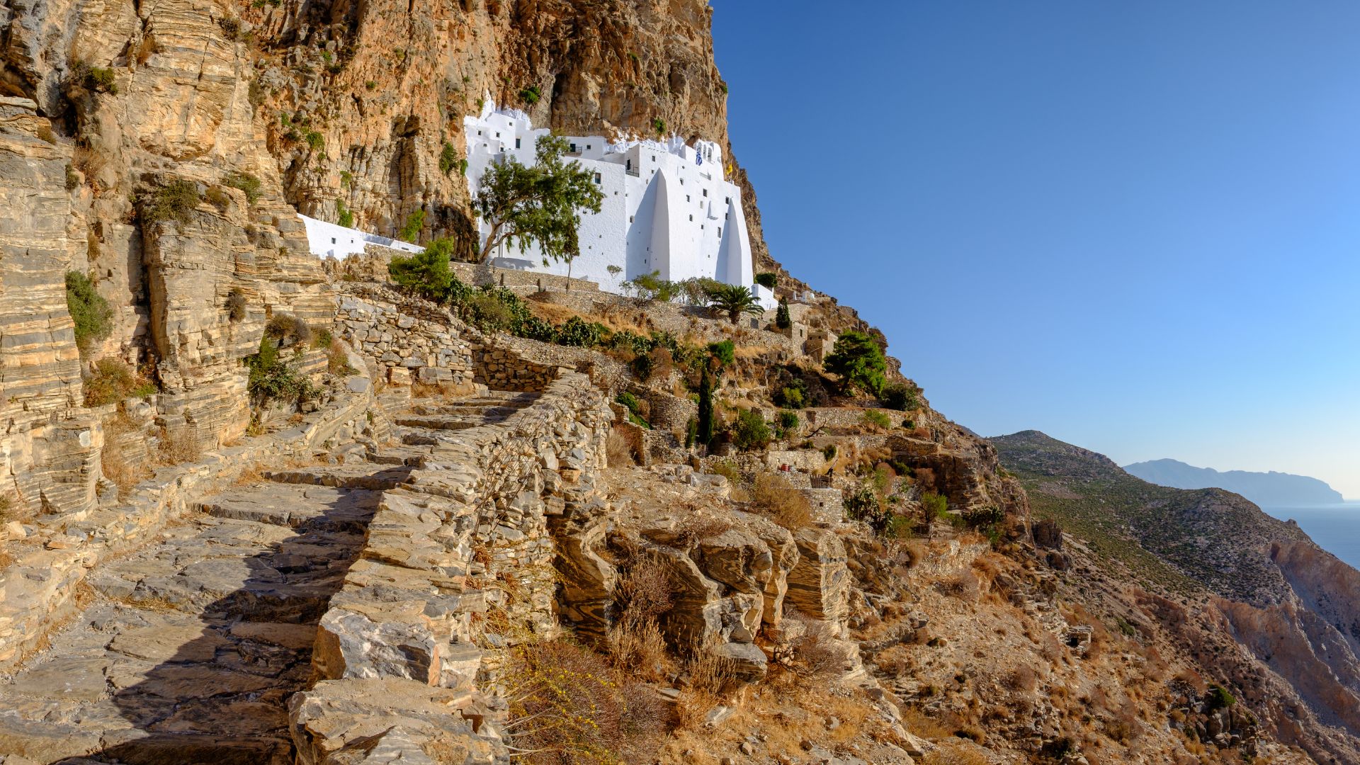 A stone kalderimi winds up a steep cliff face towards the white Panagia Hozoviotissa Monastery on Amorgos Island.