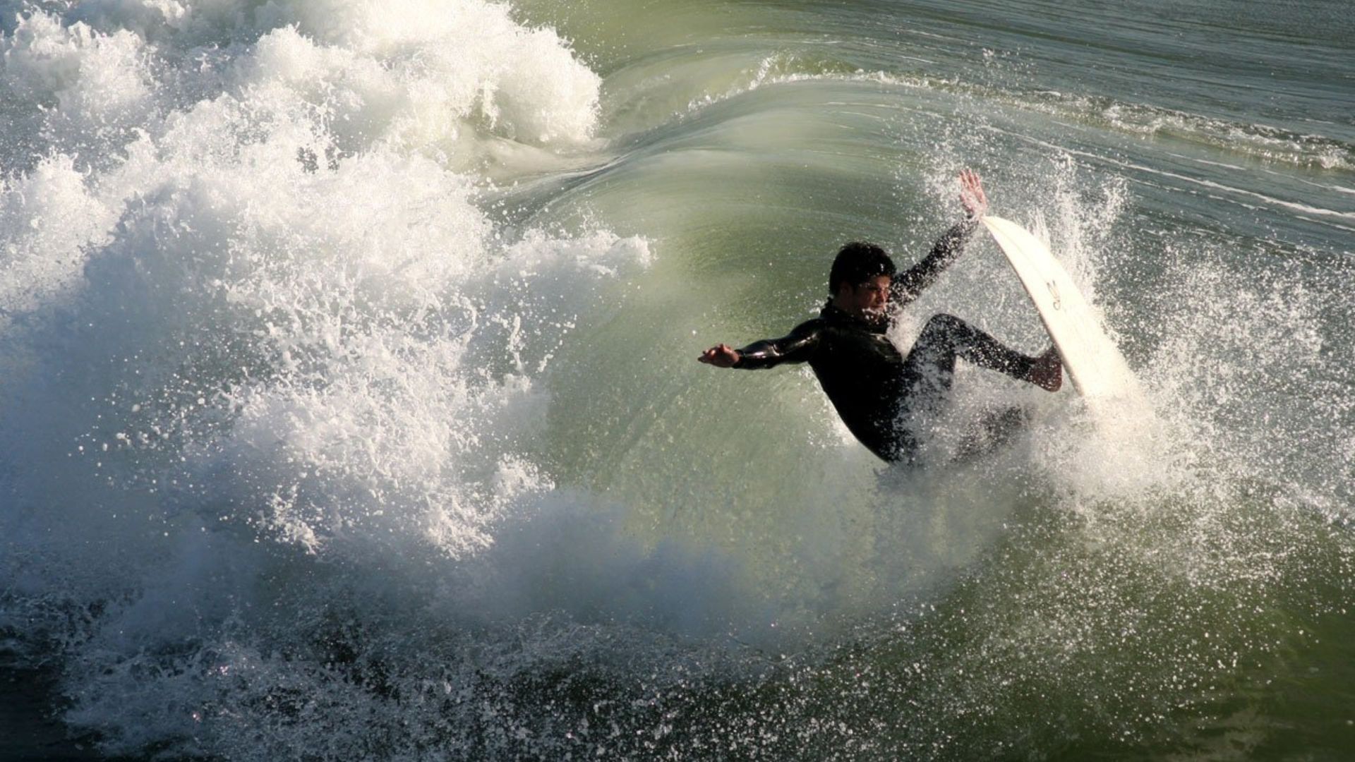 Surfer riding a powerful ocean wave at Huntington Beach Pier, California – action shot of a male surfer in a black wetsuit on a surfboard