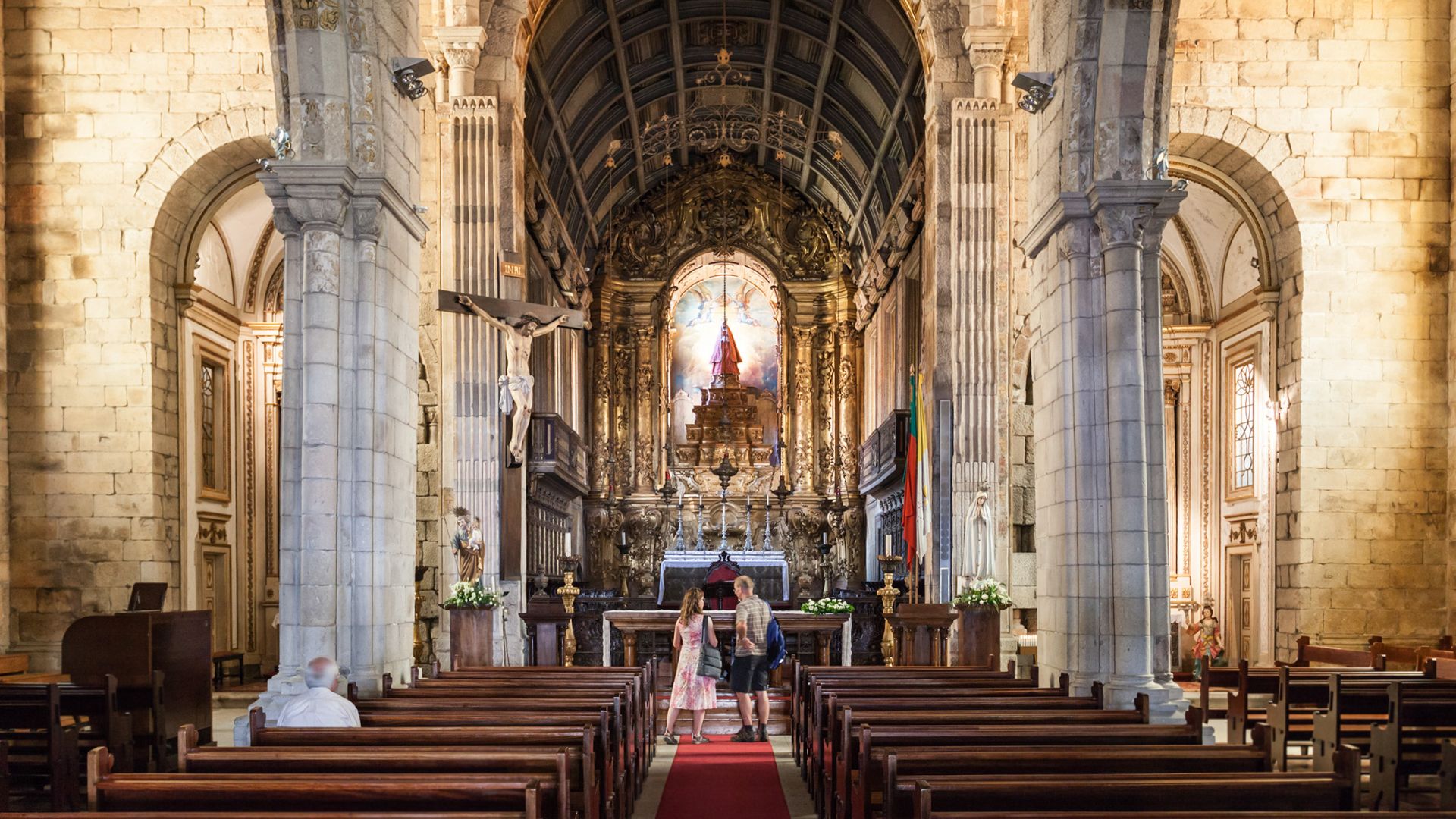 Interior view of Igreja de Nossa Senhora da Oliveira in Guimarães, Portugal, showing the main altar and nave with wooden pews.
