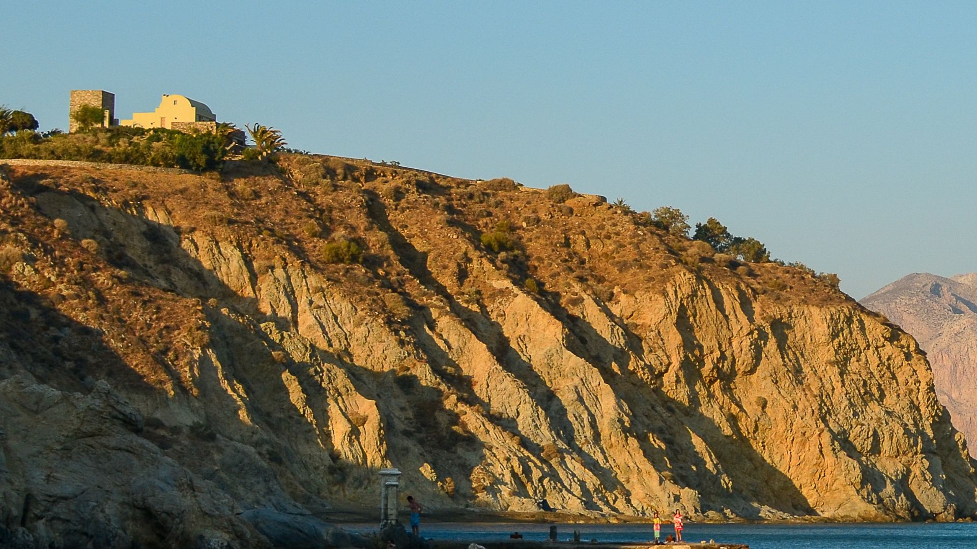 Scenic view of a rugged coastal landscape with a winding dirt road leading towards the sea under a blue sky with scattered clouds.