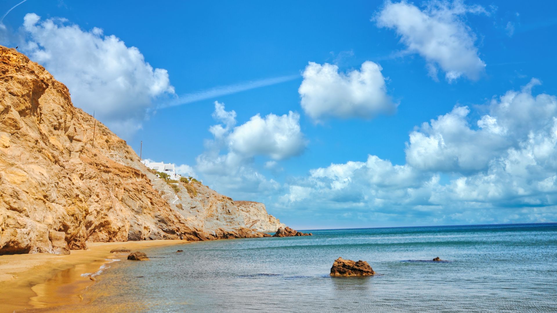Anafi, Greece beach with sandy shore, clear blue water, and rocky cliffs under a bright sky.