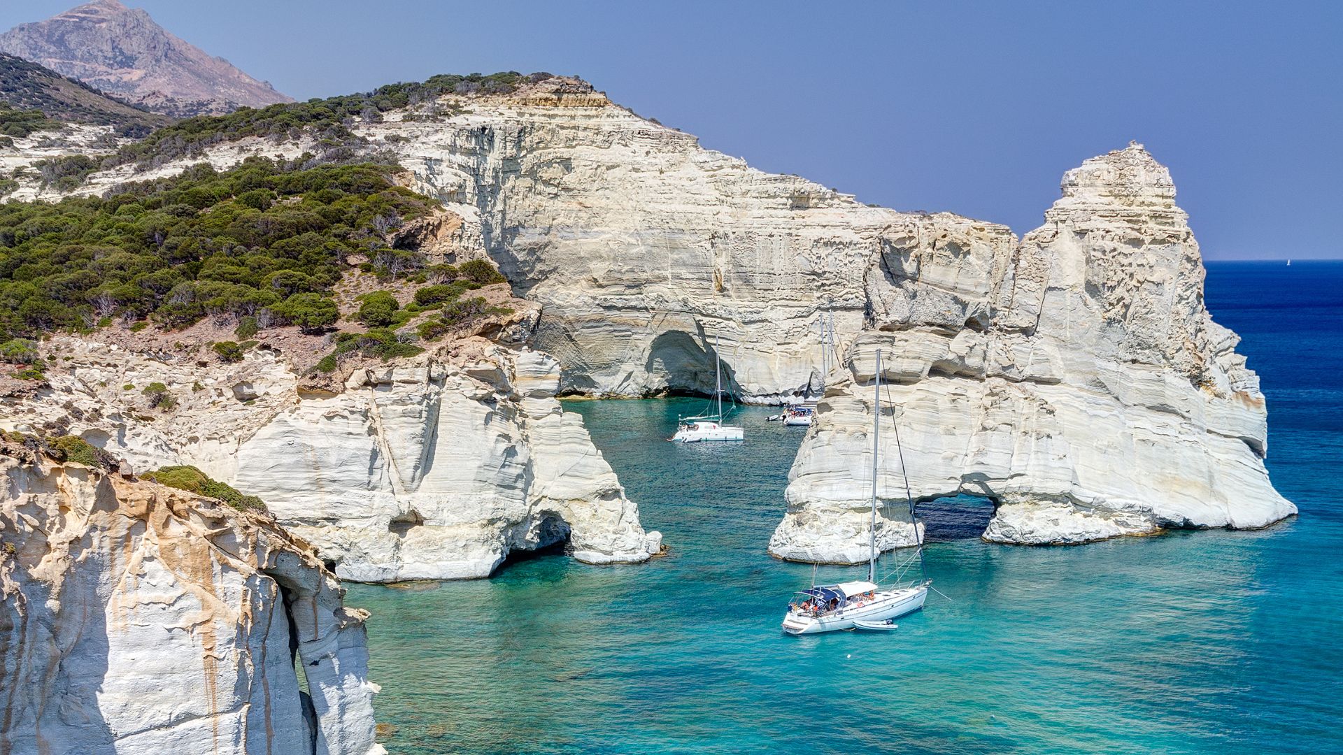 Turquoise water, rock formations,  white cliffs, and boats at Kleftiko Beach in Milos, Greece.