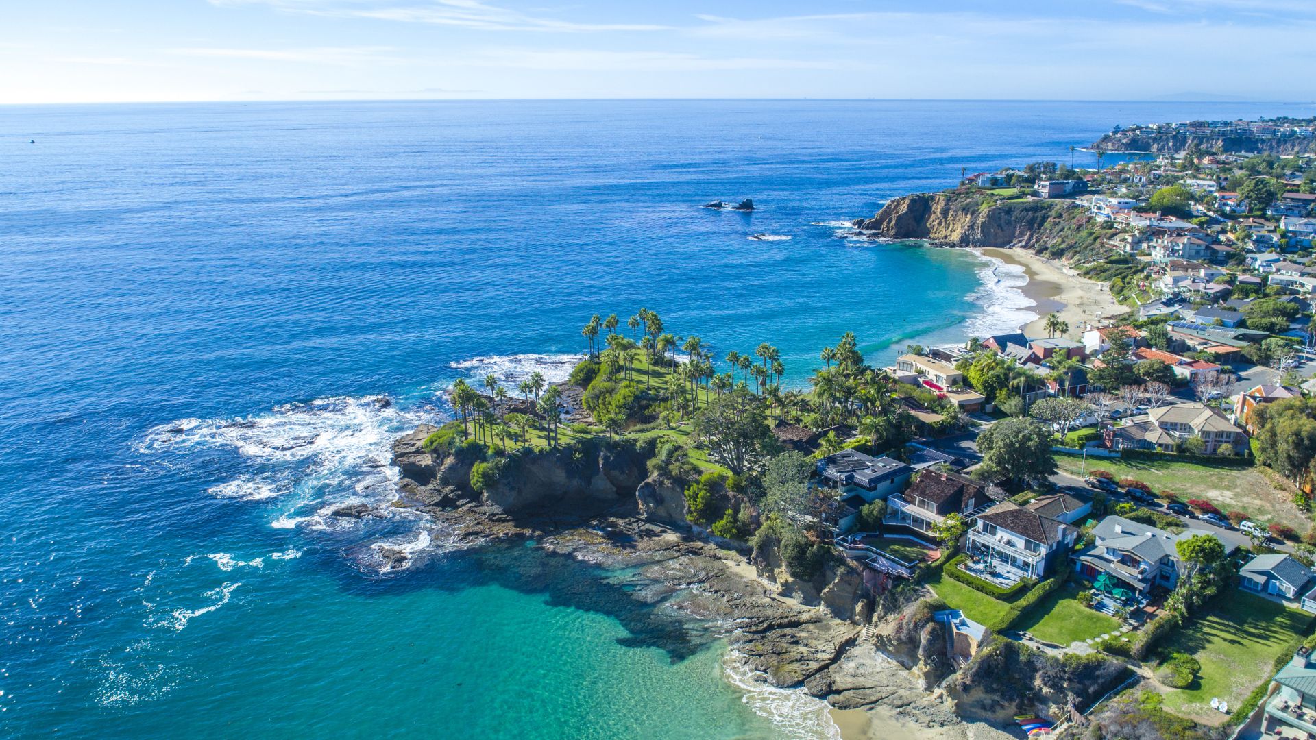 Aerial view of Laguna Beach, California, showcasing the scenic coastline, sandy beaches, turquoise ocean, and a residential area nestled along the cliffs in Orange County.