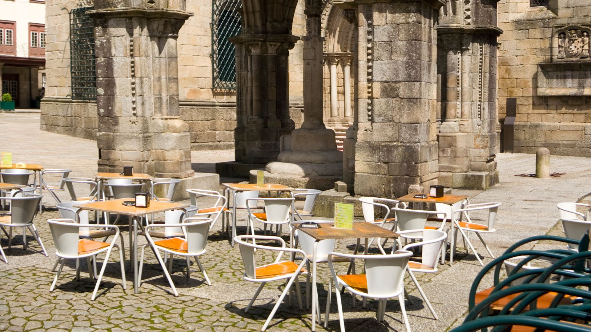 Outdoor cafe tables in a historic square with a stone church and Gothic monument in Guimarães, Portugal.