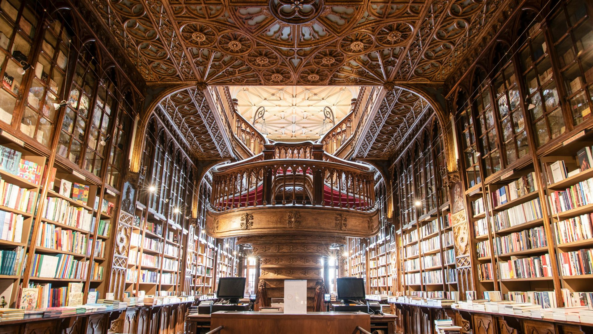 A wide shot of Livraria Lello's interior showcasing its ornate wooden staircase, bookshelves filled with books, and a wooden carve ceiling