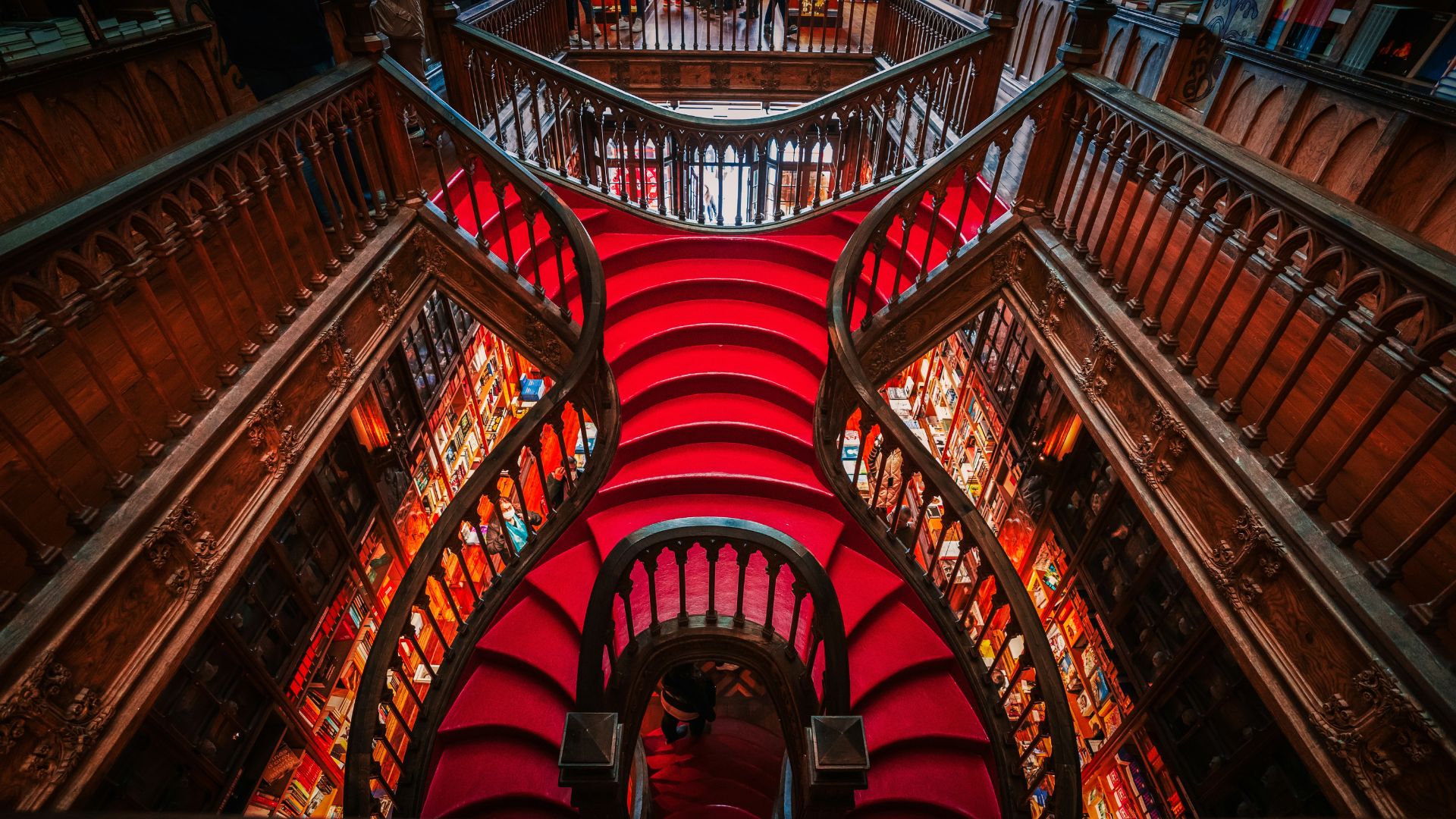 A wide shot of Livraria Lello's interior showcasing its ornate wooden staircase and bookshelves filled with books.