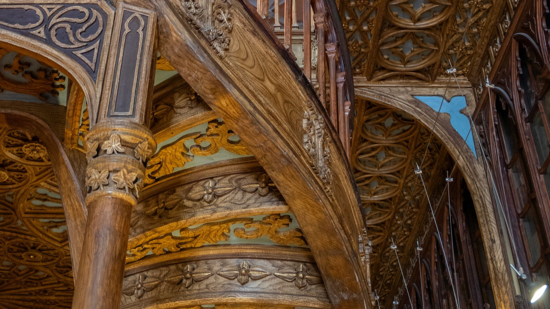 A close-up shot of the ornate wooden staircase inside Livraria Lello, with detailed carvings and a view of the ceiling.