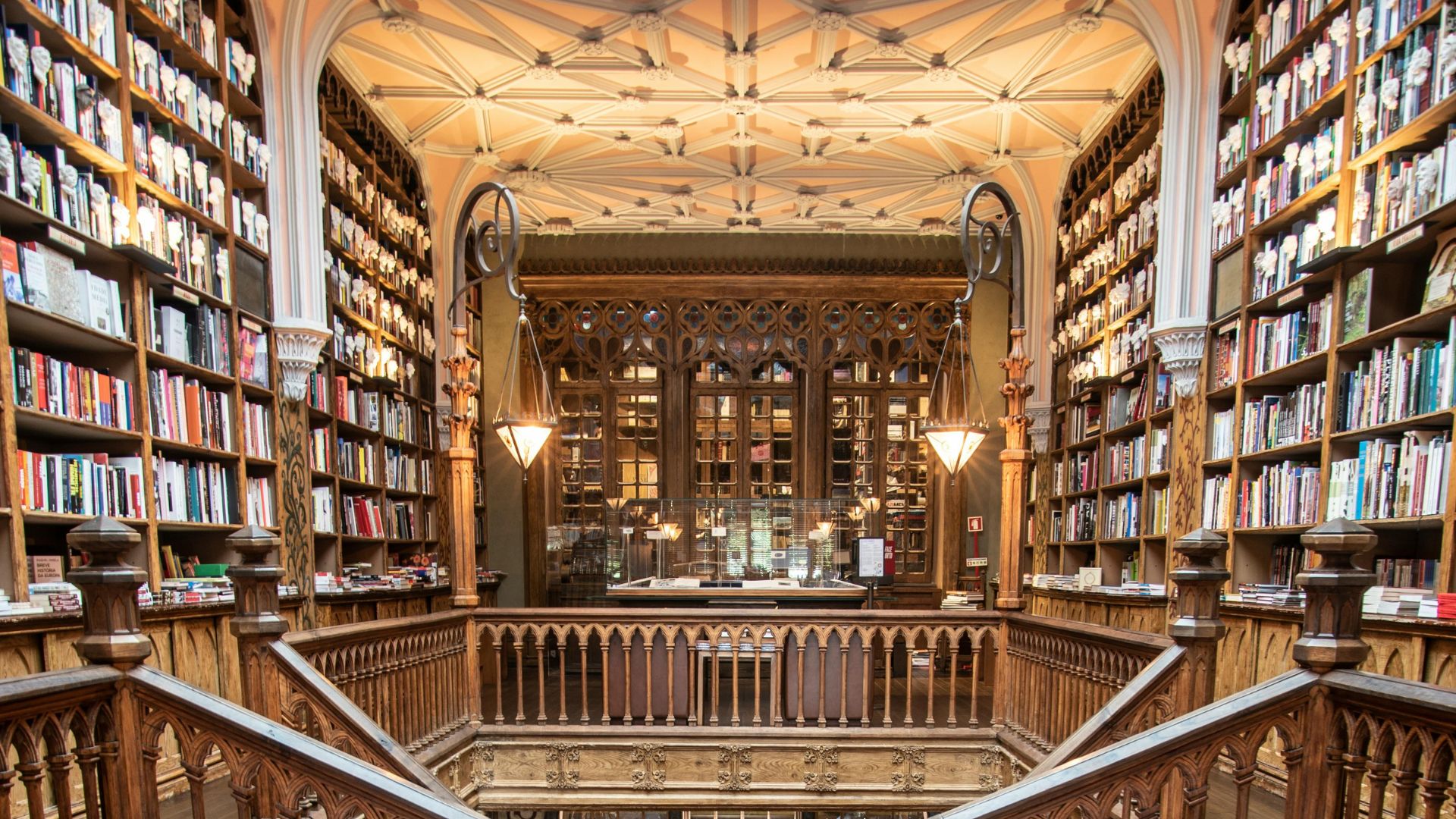 A wide shot of Livraria Lello's interior showcasing its ornate wooden staircase, bookshelves filled with books, and wooden carve ceiling.