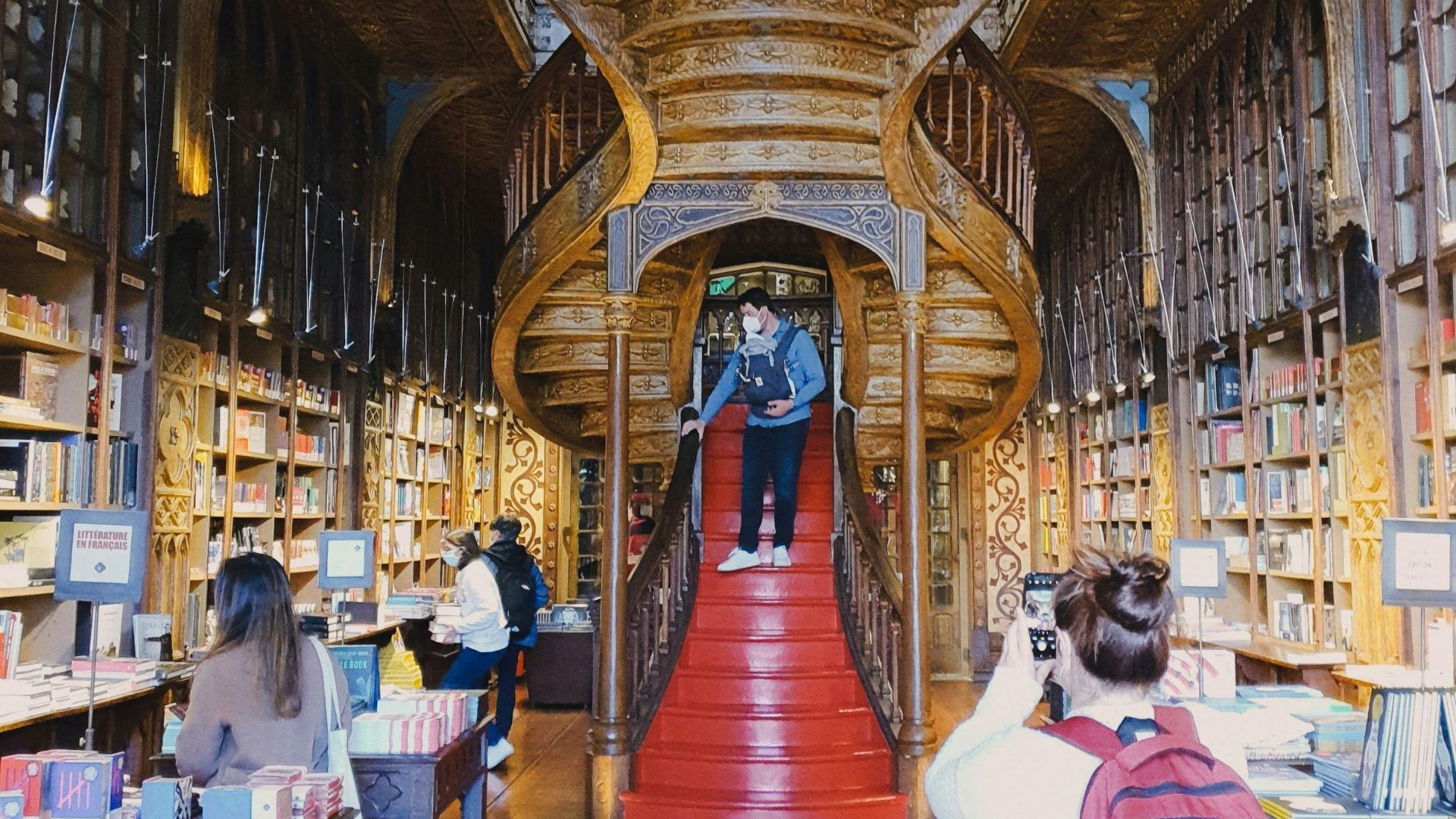 A wide shot of Livraria Lello's interior showcasing its ornate wooden staircase, bookshelves filled with books, and people.