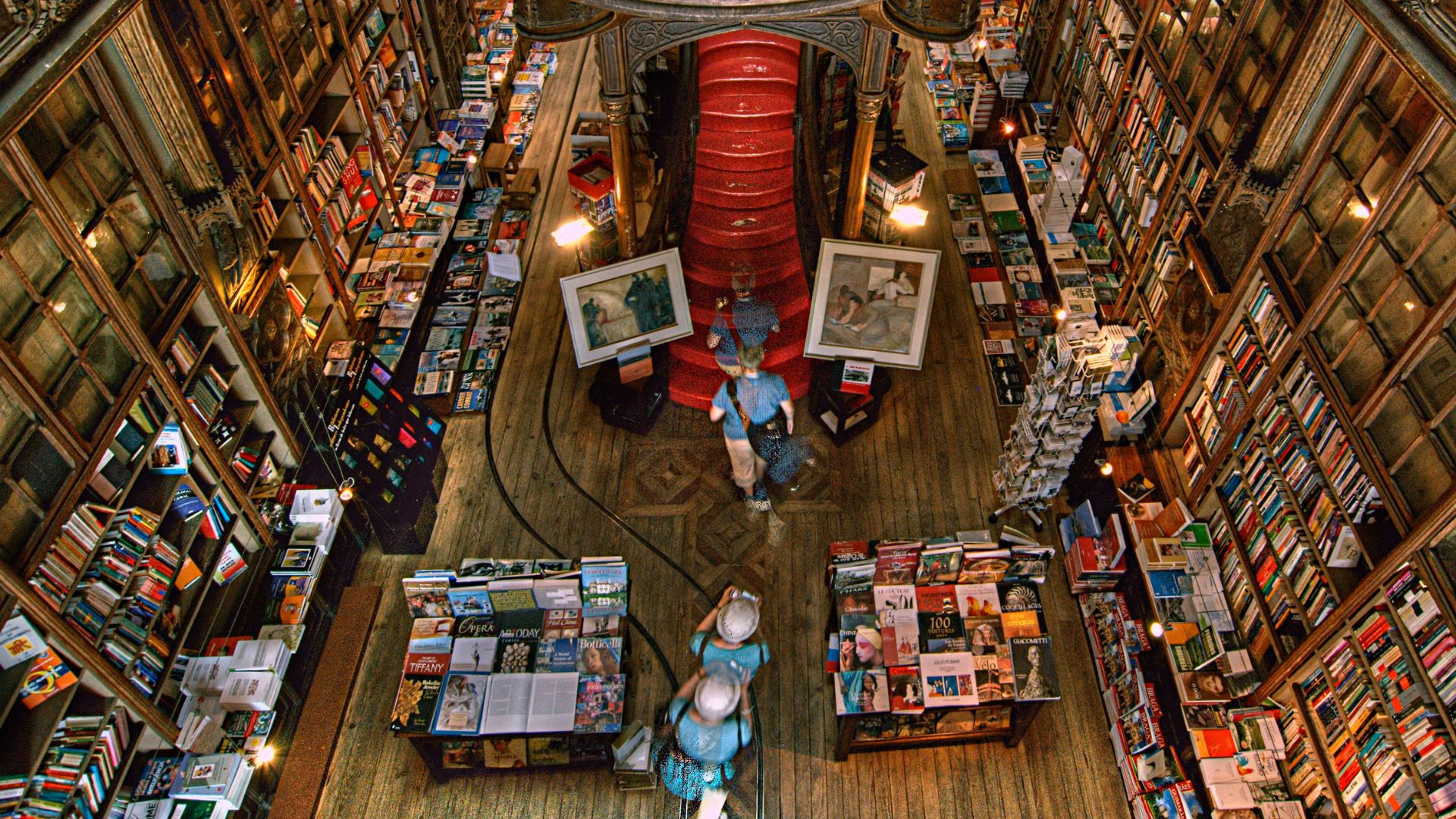 Aerial shot of Livraria Lello's interior showcasing its ornate wooden staircase, bookshelves filled with books, and people.