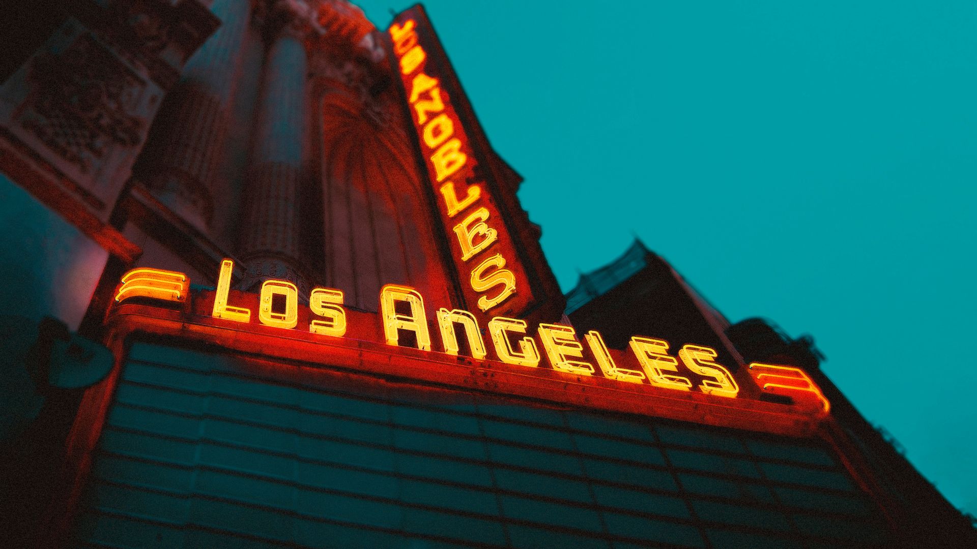 A vibrant, angled shot of a neon sign displaying 'Los Angeles' in bright orange against a dark blue sky. This eye-catching image captures the iconic signage of Los Angeles, California, known for its entertainment industry and sunny weather.