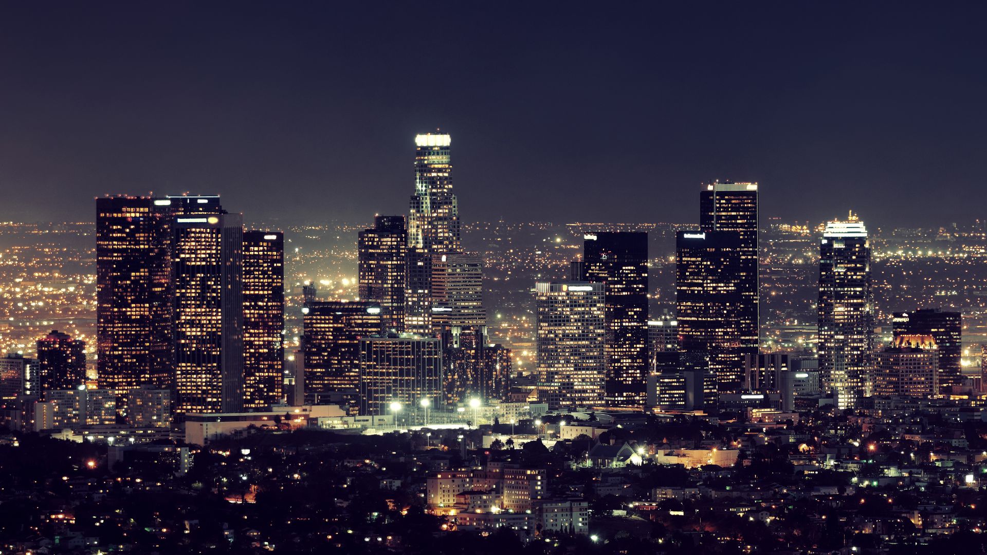 Nighttime view of the Los Angeles skyline, showcasing illuminated skyscrapers against a dark sky, capturing the city's urban landscape.