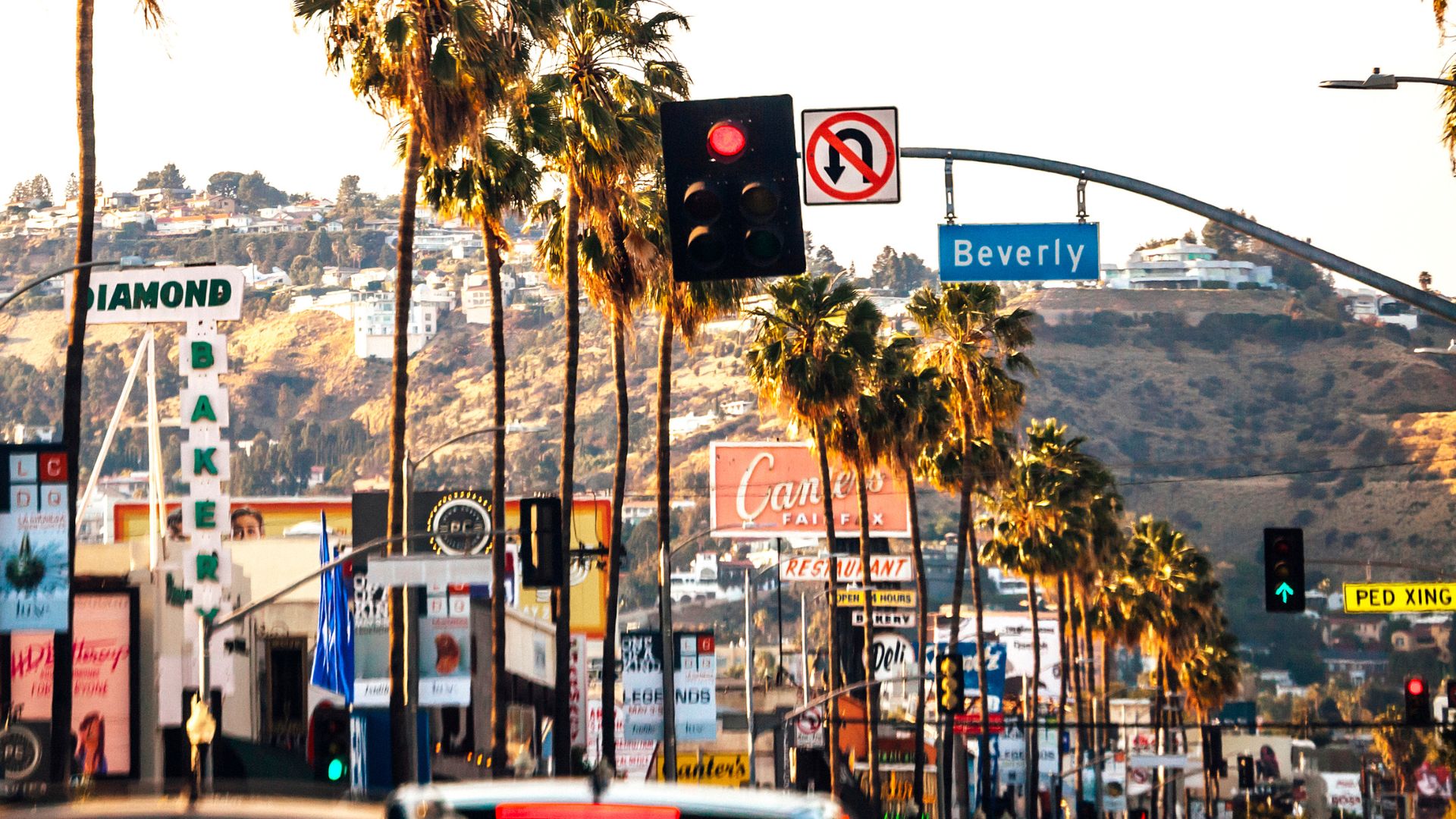 A vibrant street scene in Beverly Hills, Los Angeles, featuring palm trees, storefronts like Diamond Bakery and Canter's Deli, and a 'Beverly' street sign. This image captures the iconic Southern California atmosphere.