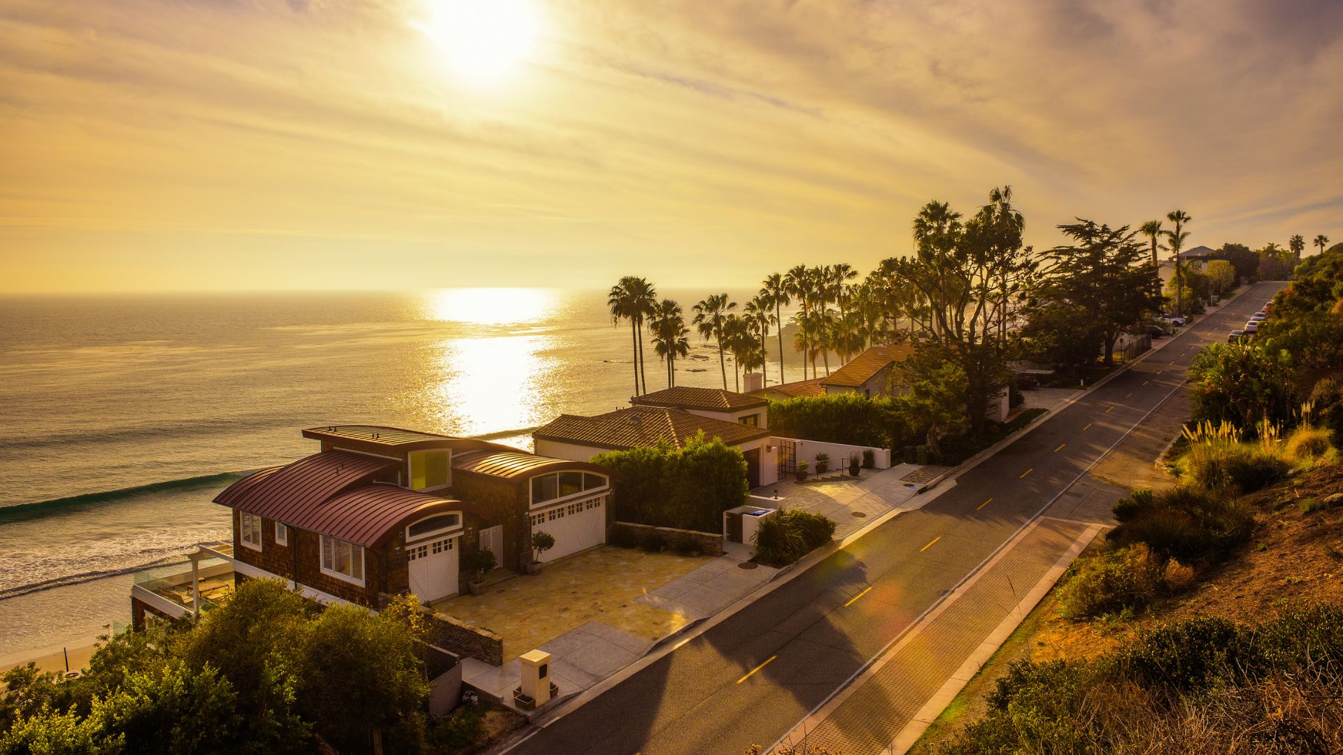Golden hour view of Malibu coastline with houses, palm trees, and Pacific Ocean.