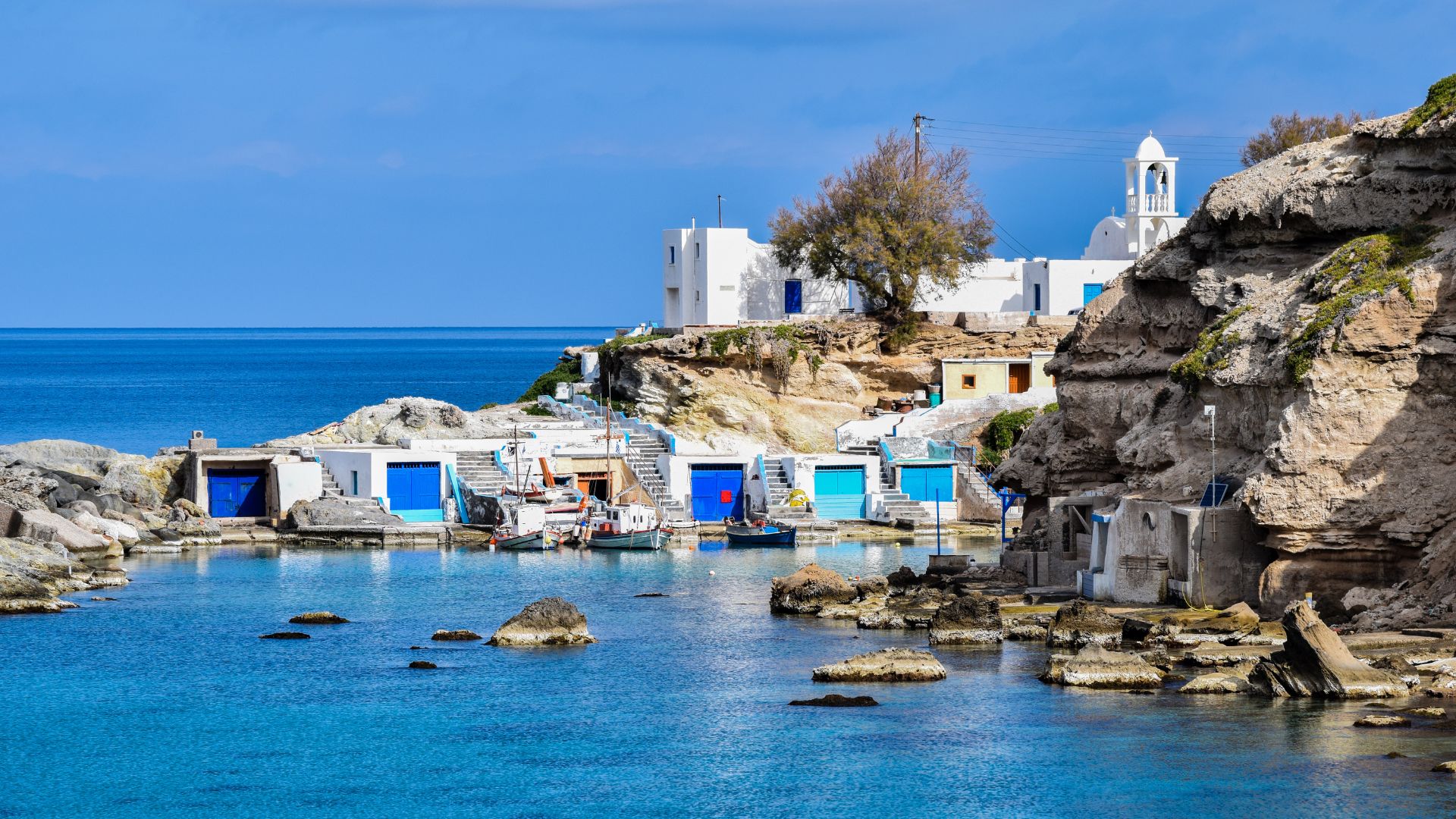 Colorful fishing village of Mandrakia in Milos, Greece, with traditional boat houses and clear blue waters.