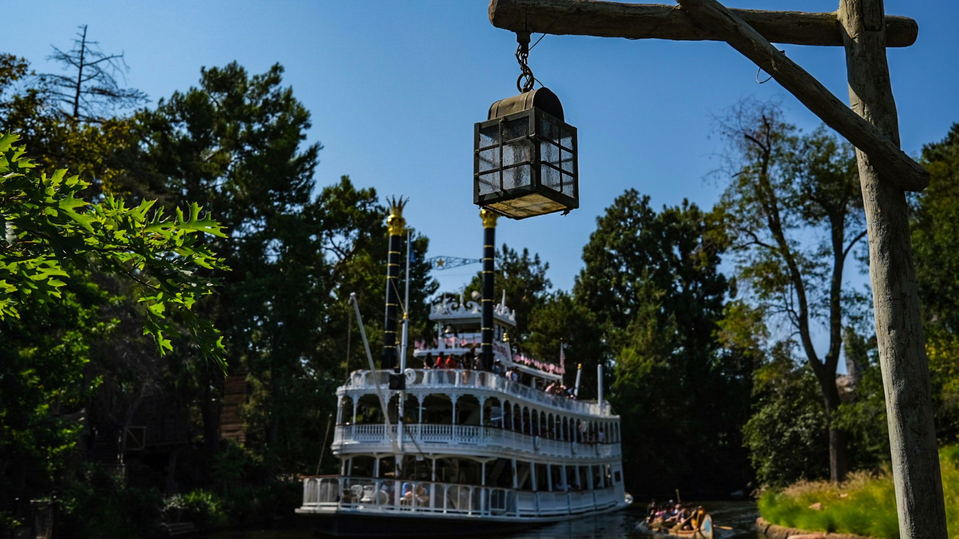 Mark Twain Riverboat sailing along the Rivers of America at Disneyland Park in Anaheim, California, with lush green trees and a clear blue sky in the background.