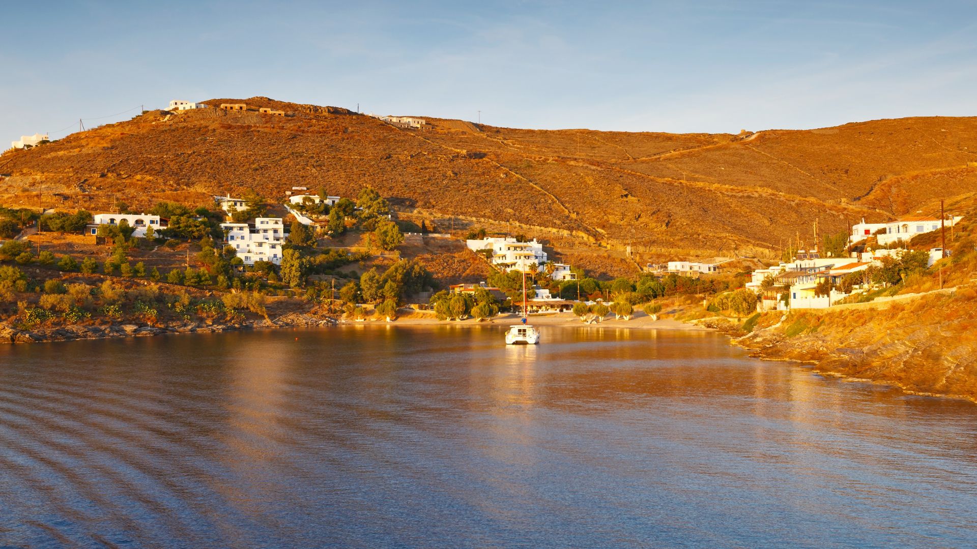 Martinakia Beach, Kythnos, Greece with calm waters, hillside homes, and a boat.