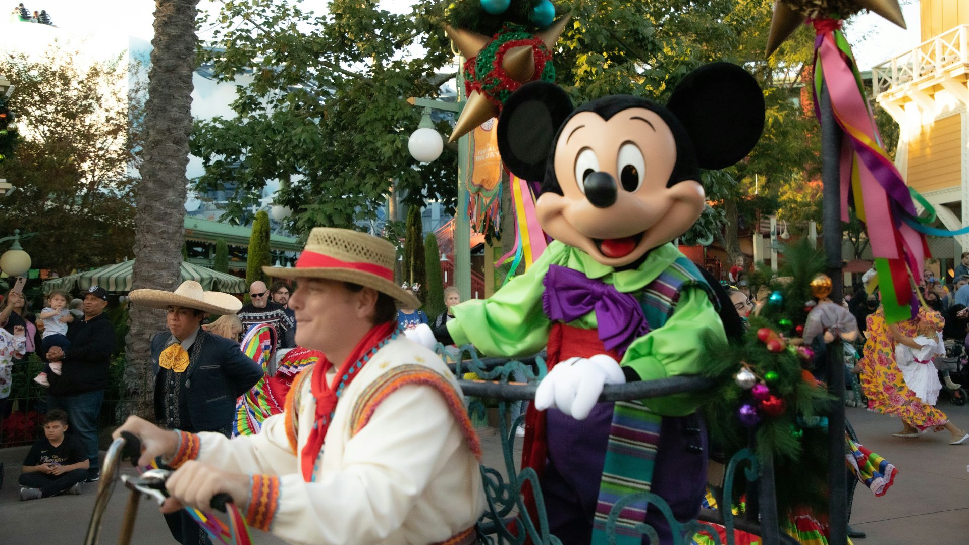 Mickey Mouse on a colorful parade float during the Disney ¡Viva Navidad! Street Party at Disney California Adventure Park, featuring festive holiday decorations and performers in traditional attire.