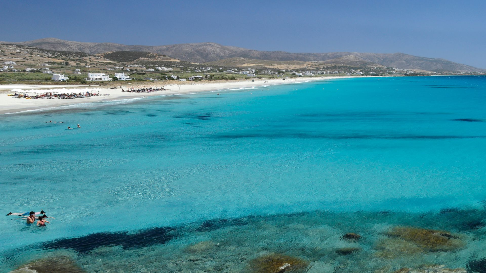 A scenic view of Mikri Vigla beach in Naxos, Greece, with turquoise waters and rocky outcrops."