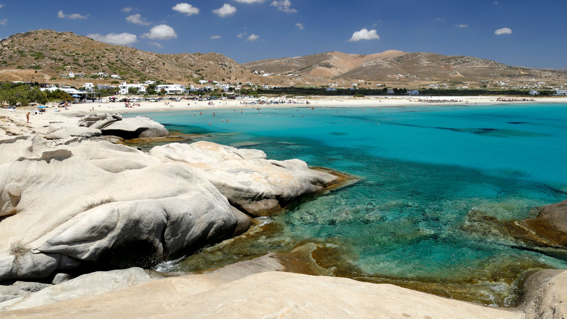 A scenic view of Mikri Vigla beach in Naxos, Greece, with turquoise waters and rocky outcrops.