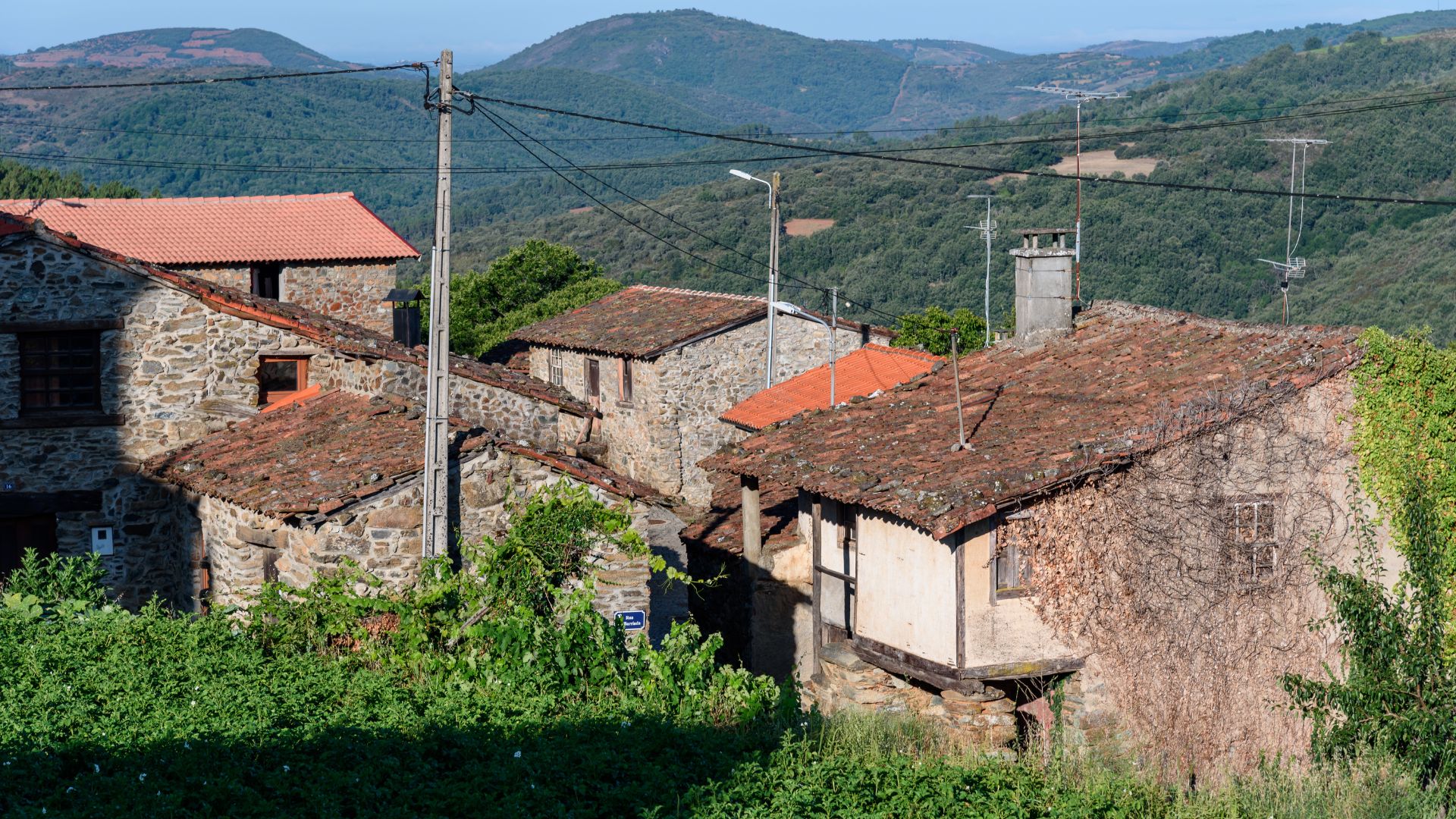 A view of a traditional stone village with red-tiled roofs nestled within a mountainous, green landscape in Montesinho Natural Park, Portugal.