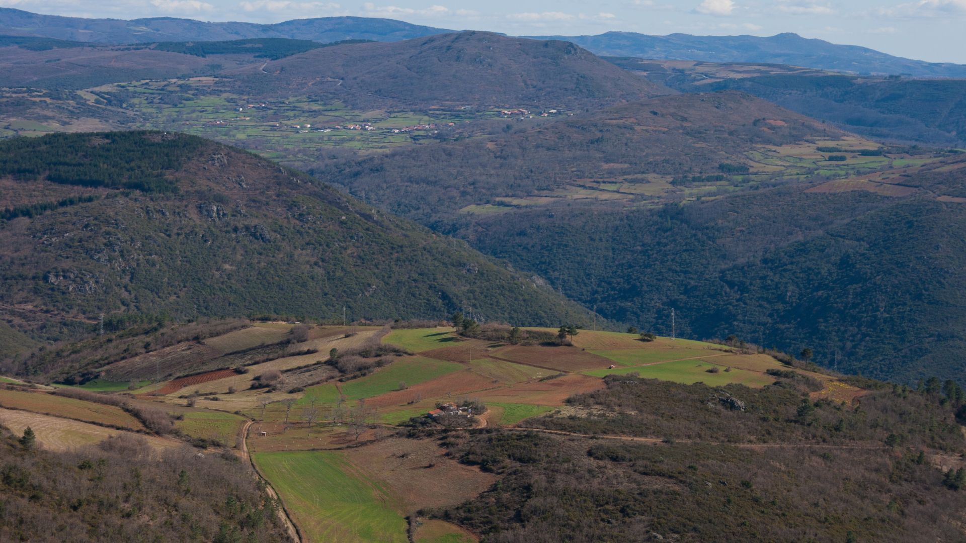 A panoramic view of the Montesinho Natural Park in Portugal, showcasing rolling hills, terraced farmlands, and forested valleys under a clear sky.