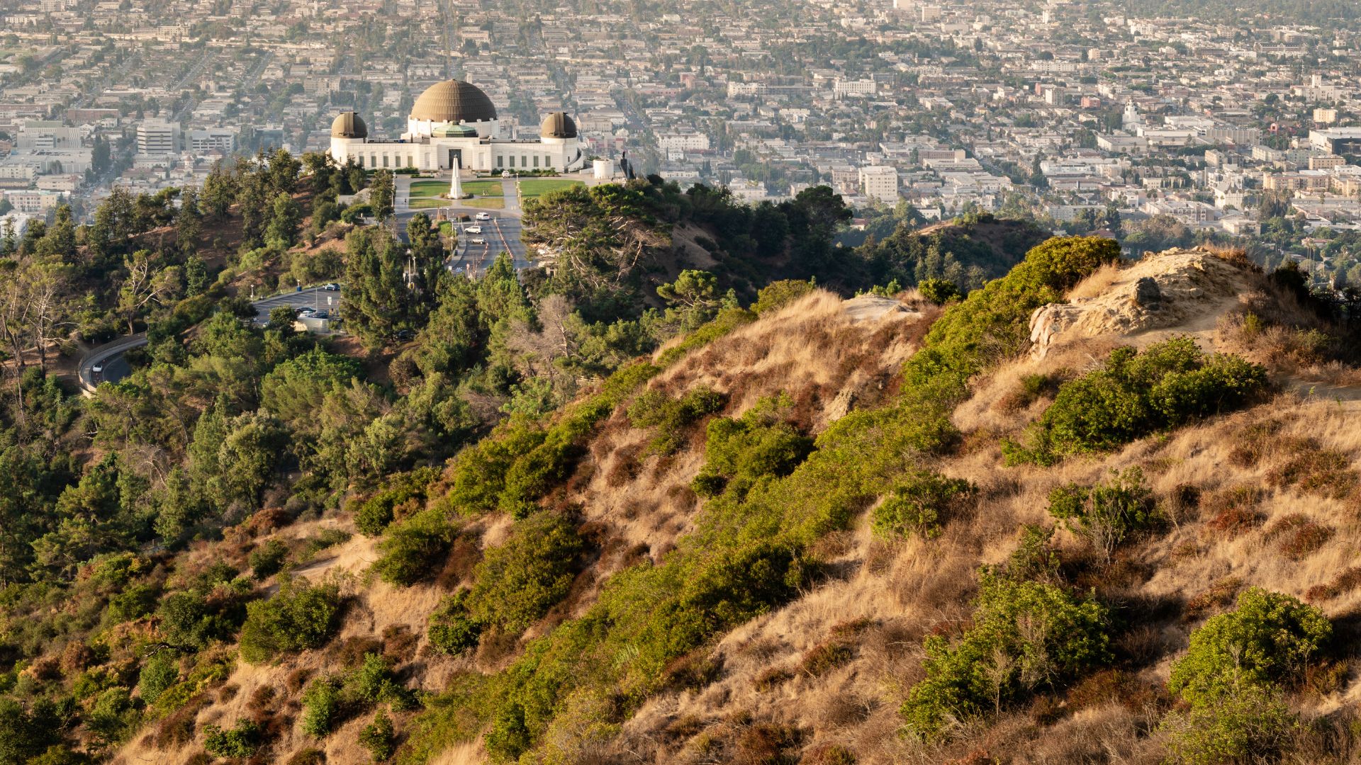 Panoramic view of Griffith Observatory on Mount Hollywood, Los Angeles, California, with hiking trails in the foreground and city skyline in the background. Ideal image for travel, hiking, and Los Angeles tourism content.
