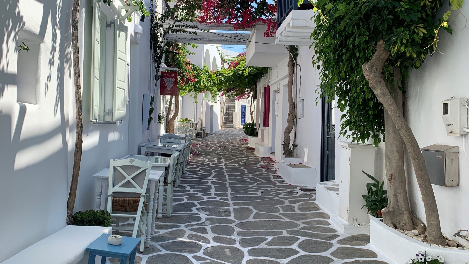 Cobblestone alley, white washed building, with tables and chairs, and bougainvilla at Paros, Greece.