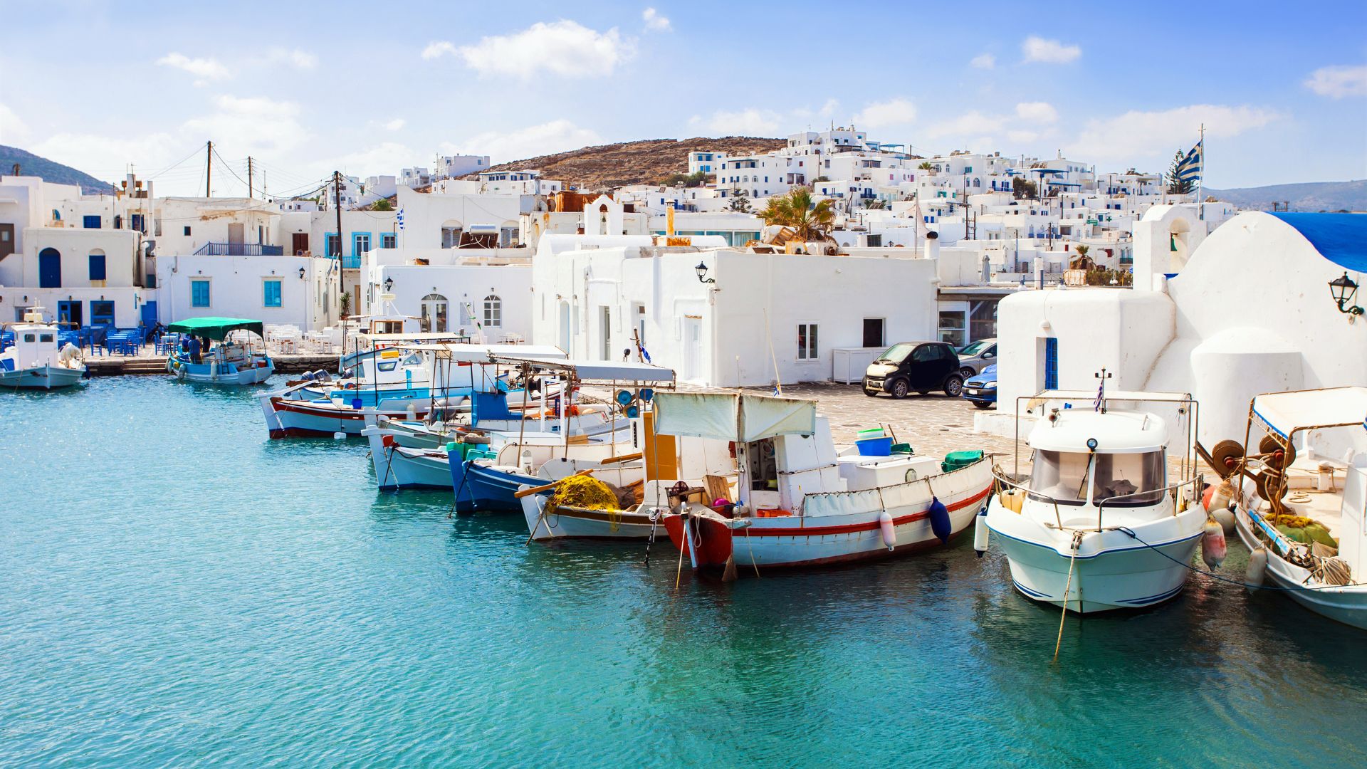 Fishing boats in a Greek harbor with white buildings in the background.