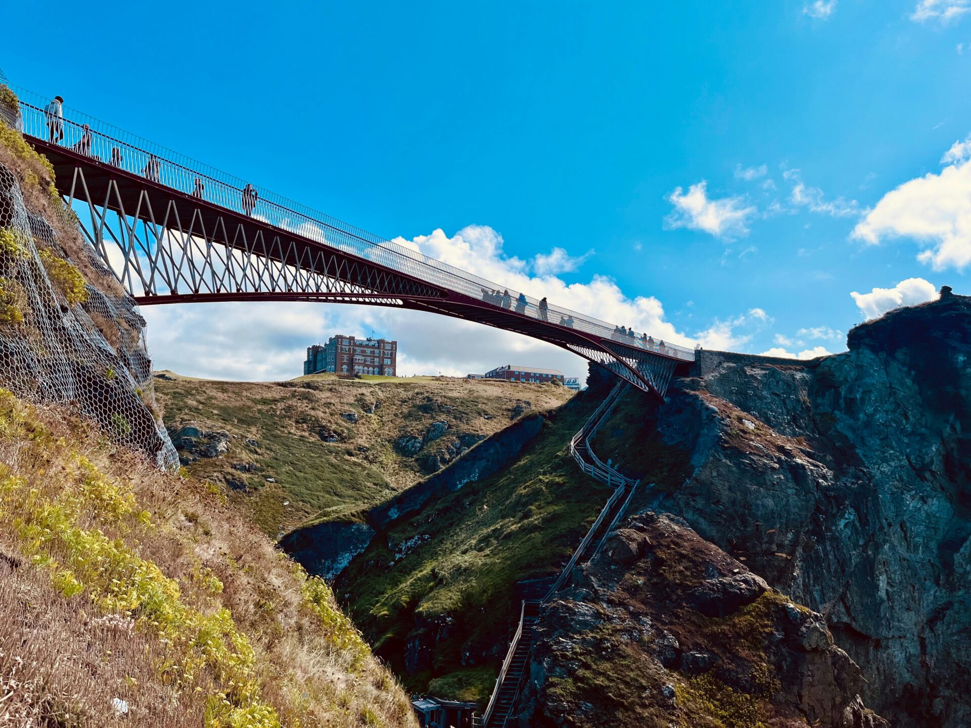 Tourists walking a hanging bridge to Tintagel Castle’s island