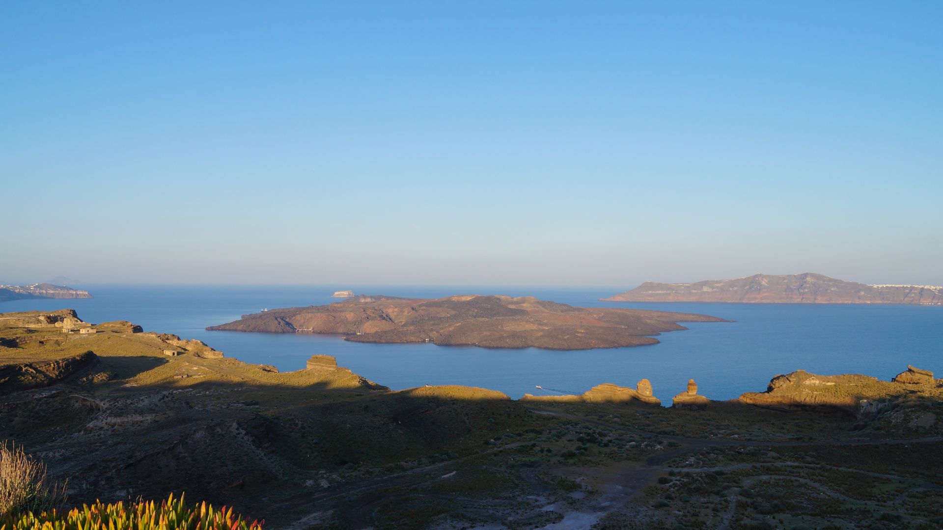 Panoramic view of Nea Kameni, a volcanic island in Santorini, with its dark lava formations surrounded by the blue Aegean Sea.