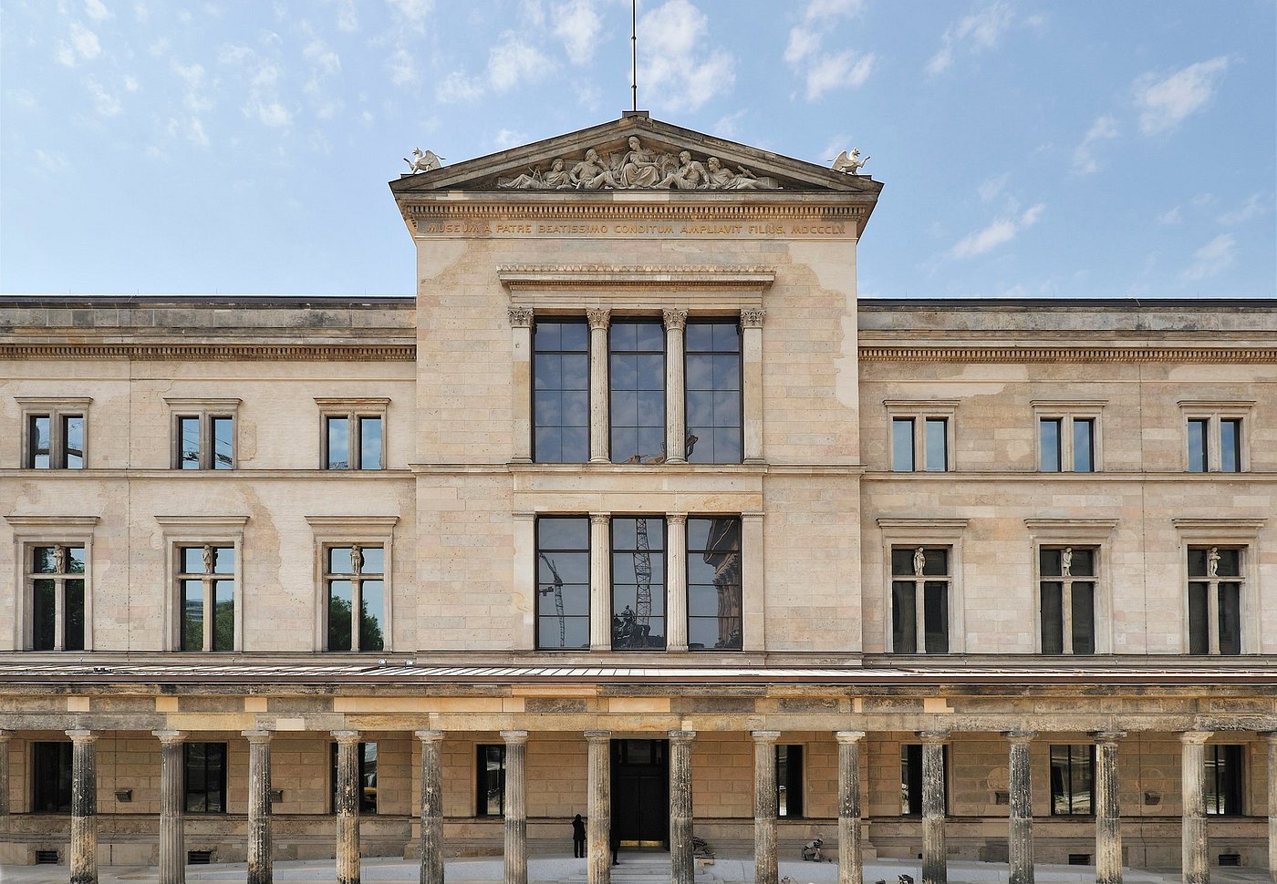 Exterior view of the Neues Museum in Berlin with classical columns and restored facade under a blue sky.