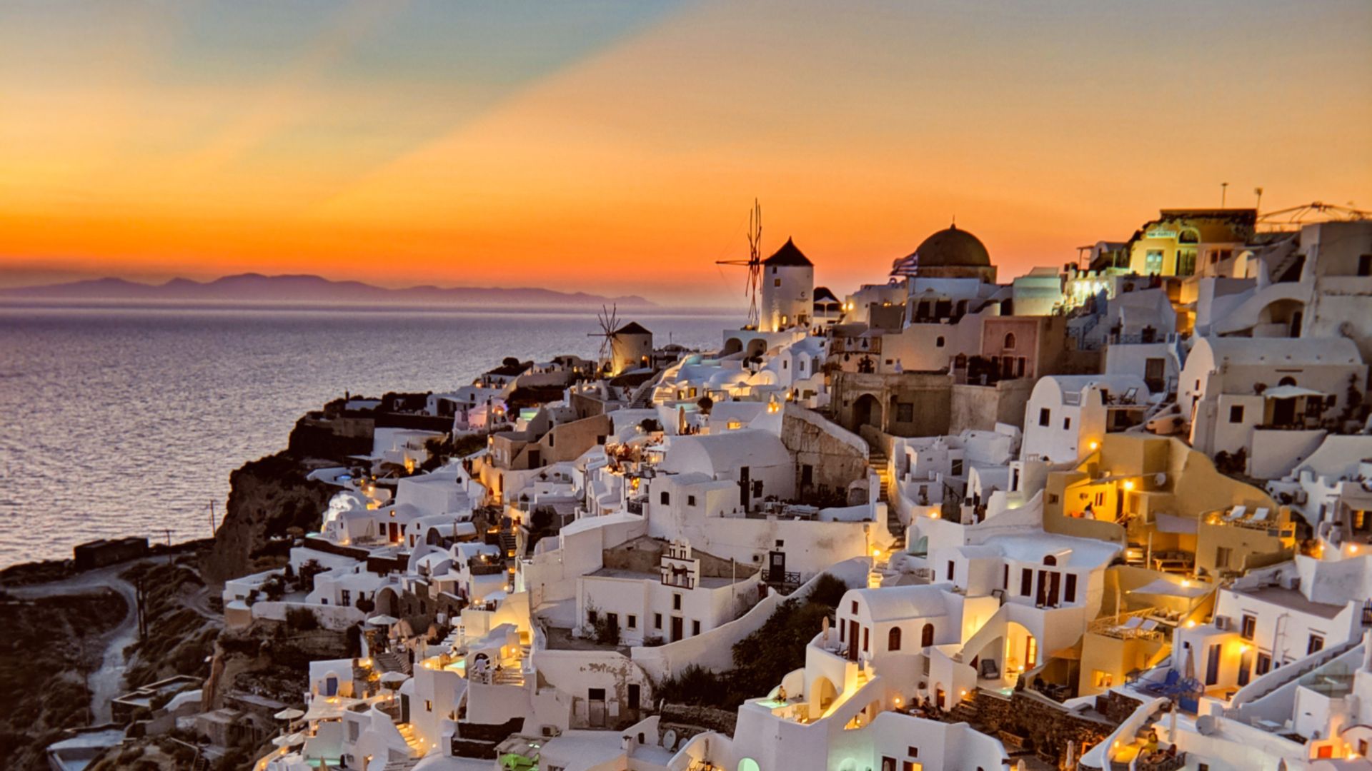 Sunset at Oia village of Santorini Islands in Cyclades, Greece featuring white washed buildings on a hill facing the sea.