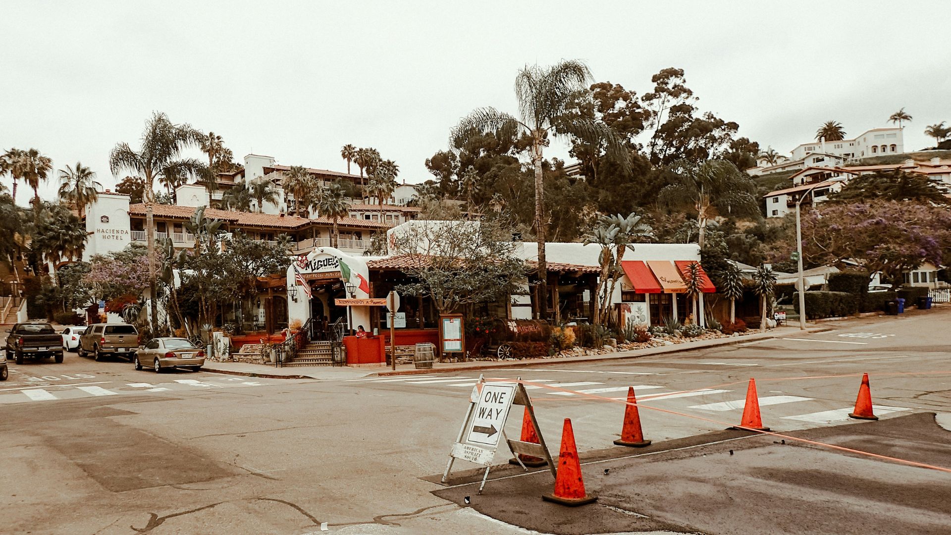 A street scene in Old Town San Diego State Historic Park, featuring historic buildings, palm trees, and a "ONE WAY" sign with traffic cones at an intersection.