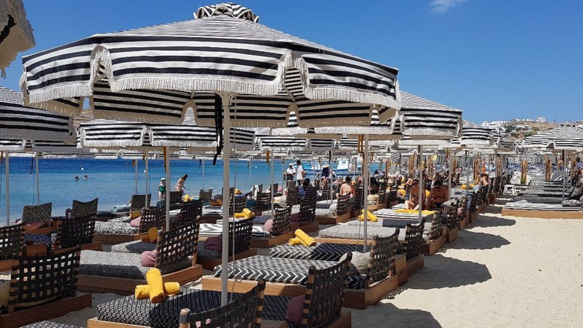 A beach with black and white striped umbrellas and lounge chairs.