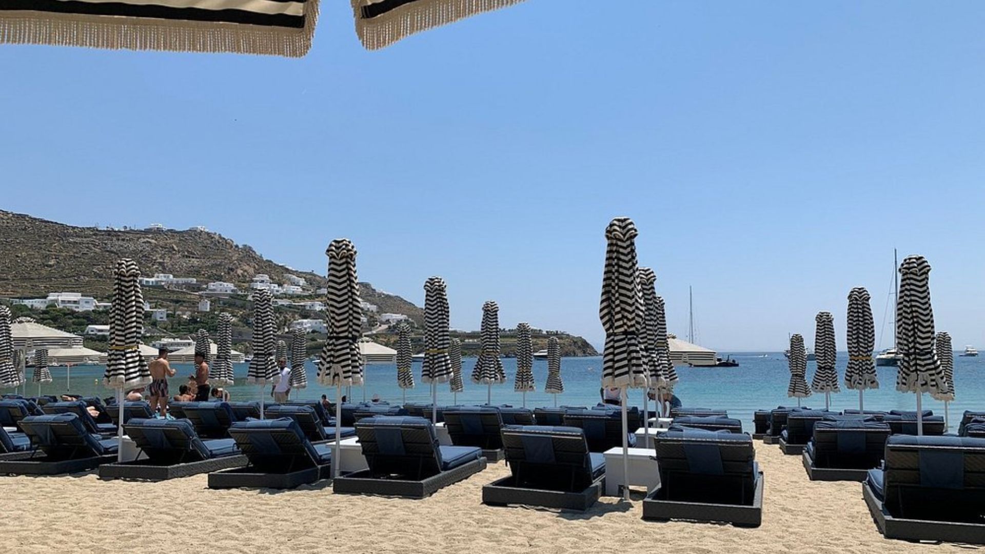 A beach with black and white striped umbrellas and lounge chairs.