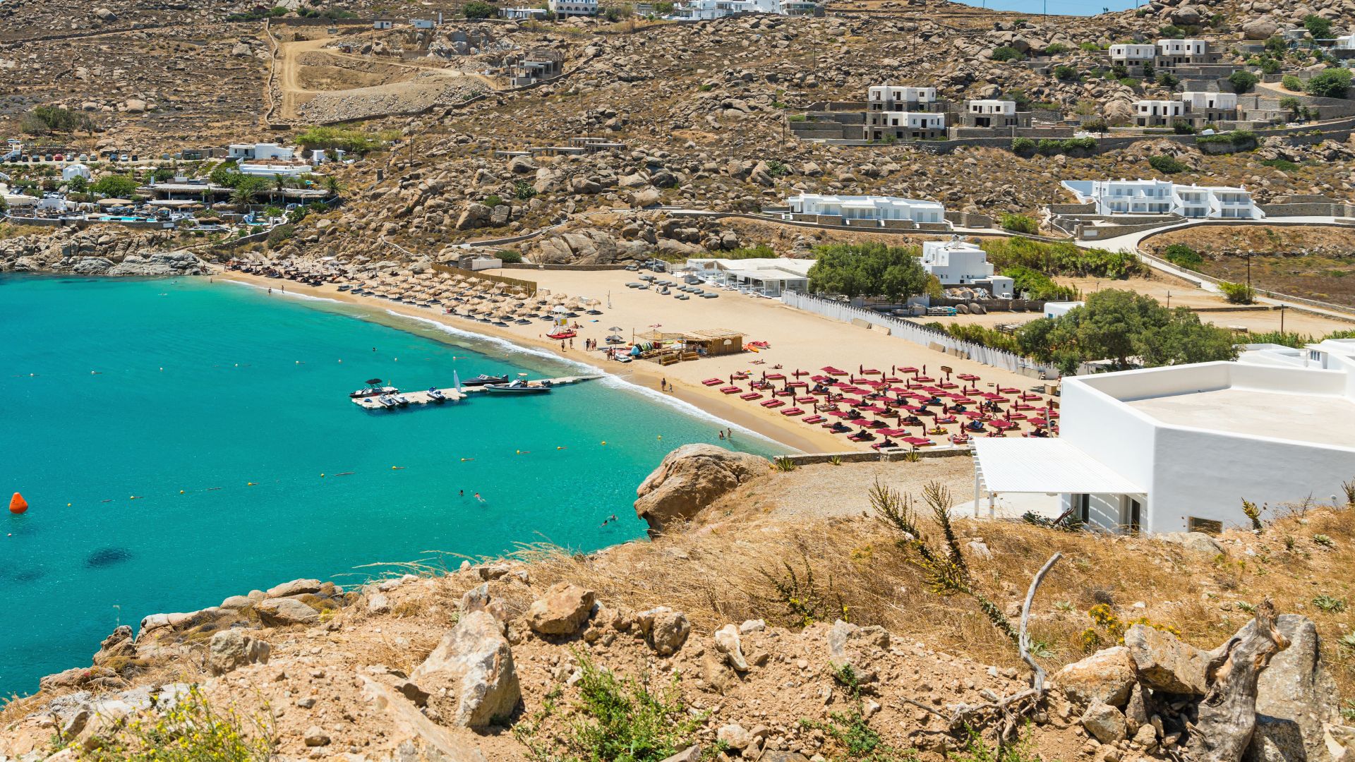 A scenic view of Paradise Beach Club in Mykonos, with turquoise water, golden sand, and beach umbrellas.