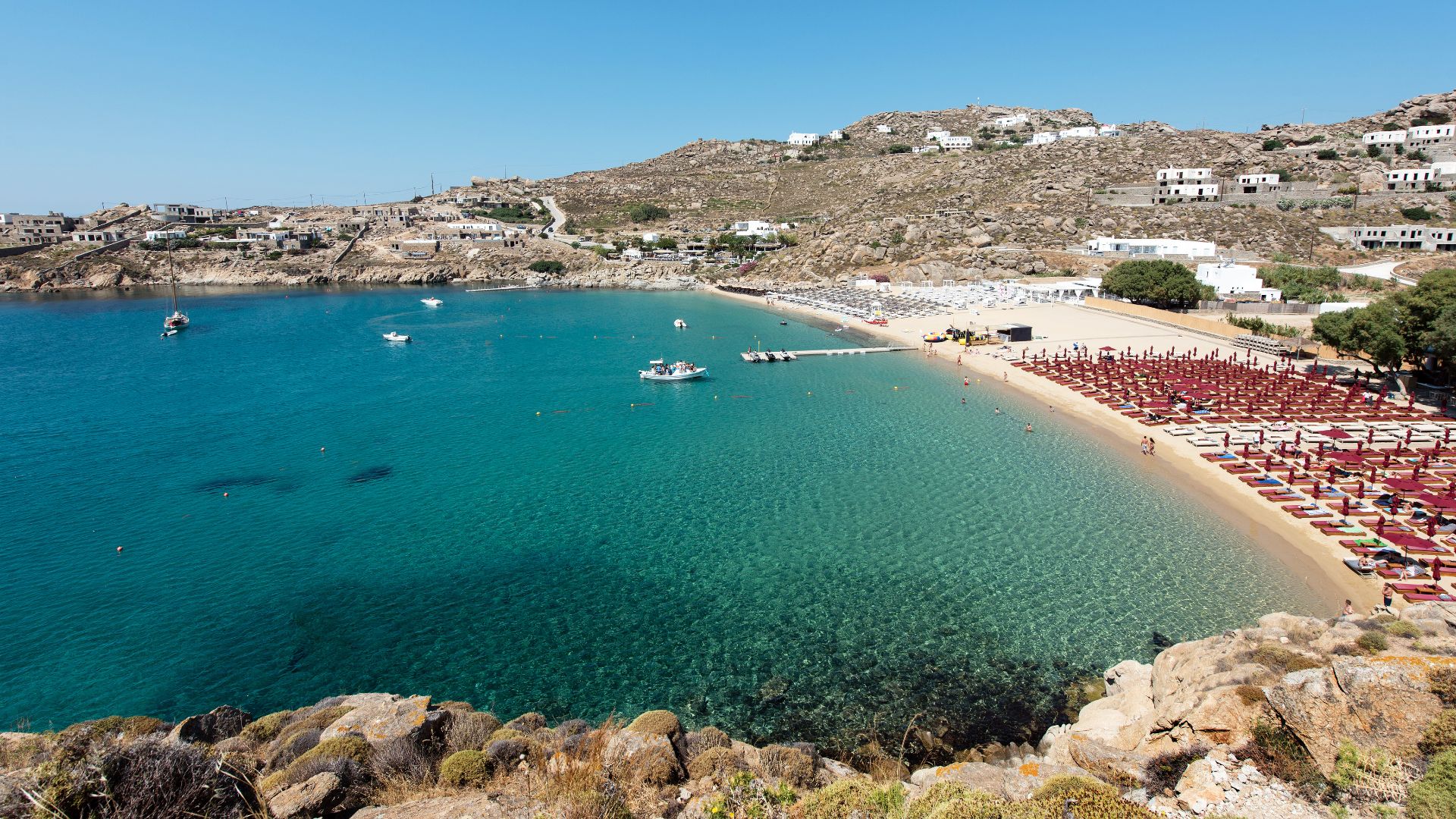 A scenic view of Paradise Beach Club in Mykonos, with turquoise water, golden sand, and beach umbrellas.