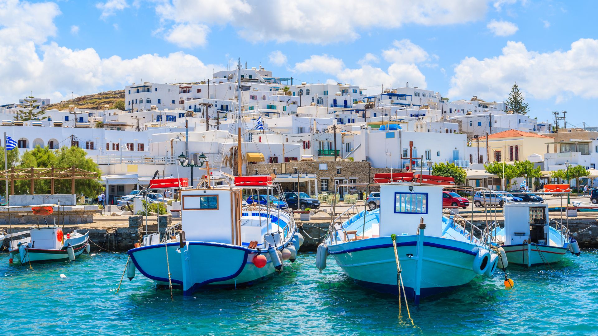 Fishing boats in the harbor of Parikia, Paros, Greece, with whitewashed buildings in the background.