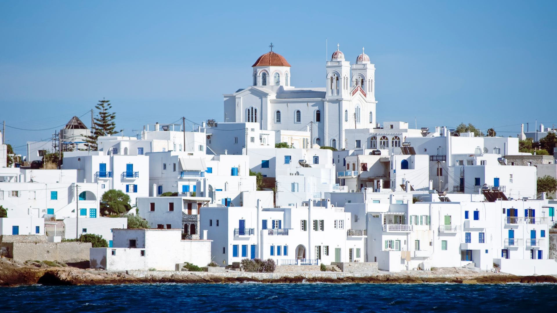 A picturesque village in Paros, Greece, with whitewashed buildings and a prominent church overlooking the sea.