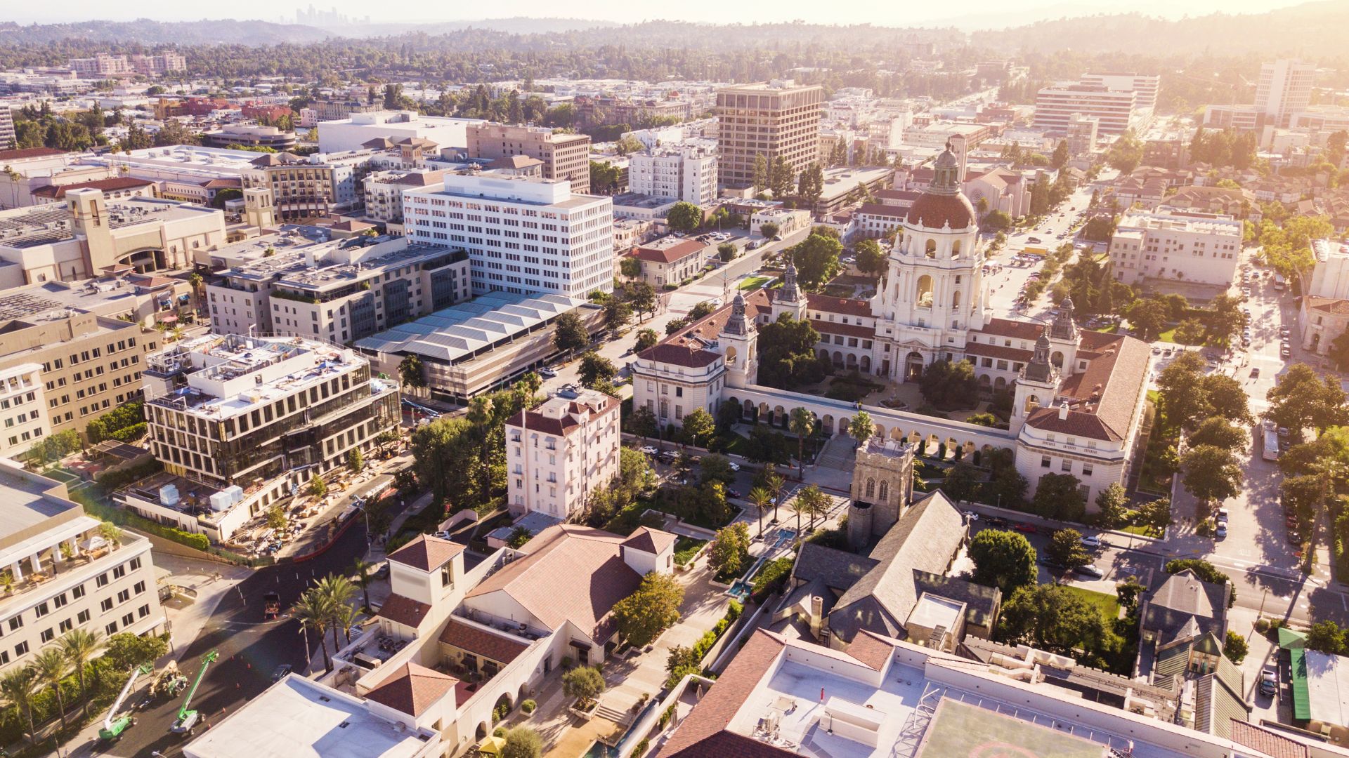 An aerial view of Pasadena City Hall and surrounding buildings at sunset, with mountains in the background.