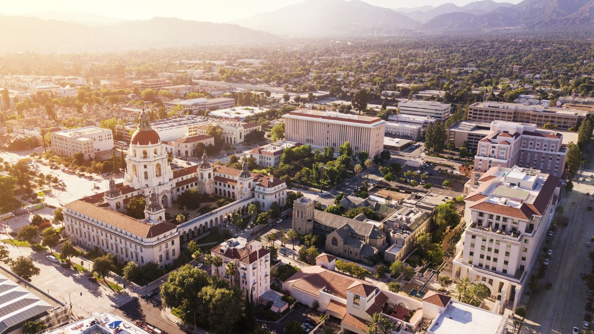 An aerial view of Pasadena City Hall and surrounding buildings at sunset, with mountains in the background.