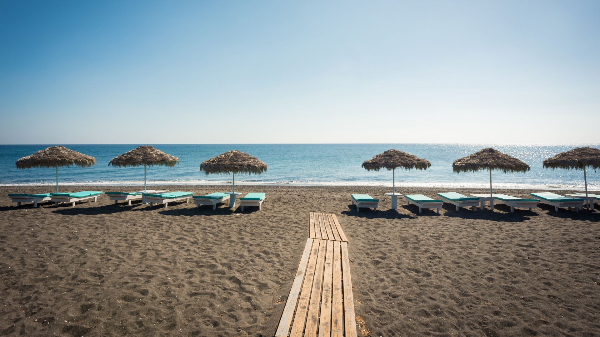 A scenic view of beach chairs and umbrellas on the black sand of Perivolos Beach in Santorini, Greece.