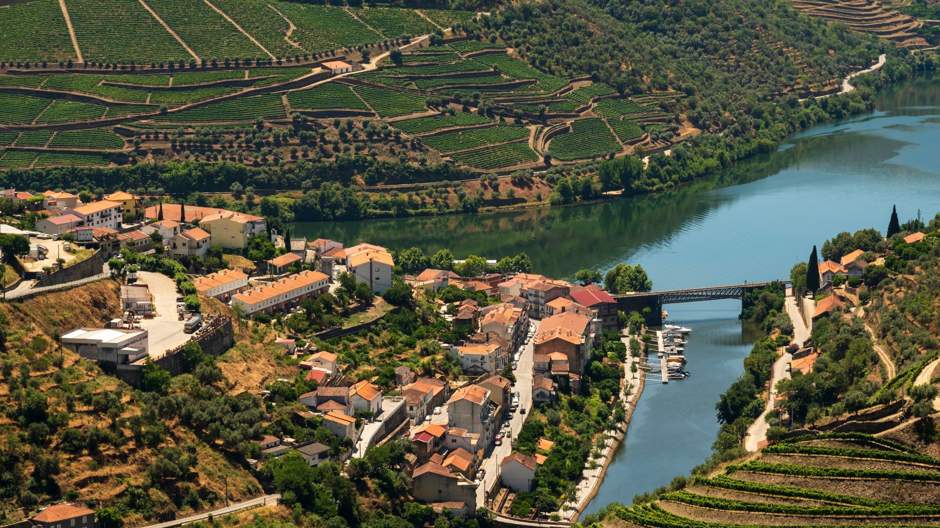 An aerial view of Pinhão, Portugal, showcasing a village nestled along the Douro River, surrounded by terraced vineyards on the hillsides.