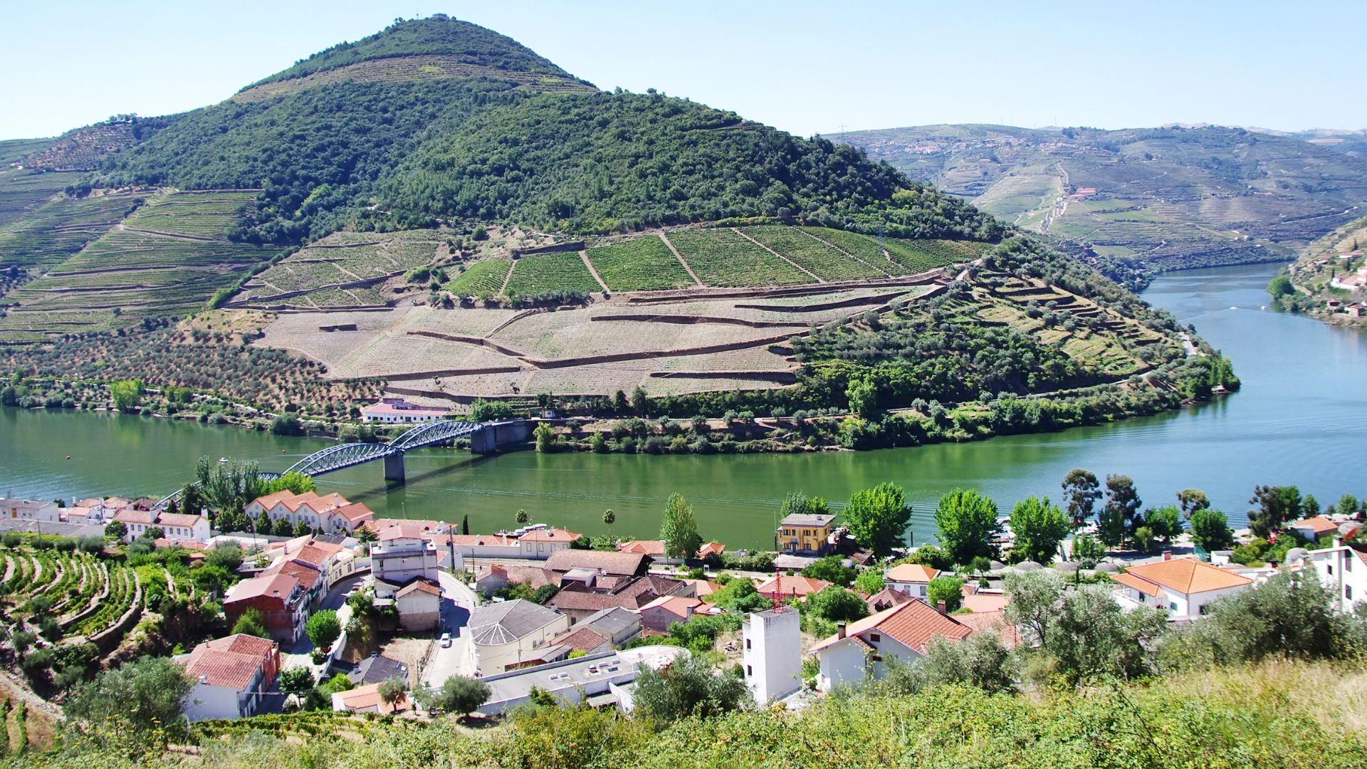 An aerial view of Pinhão, Portugal, showcasing a village nestled along the Douro River, surrounded by terraced vineyards on the hillsides. 