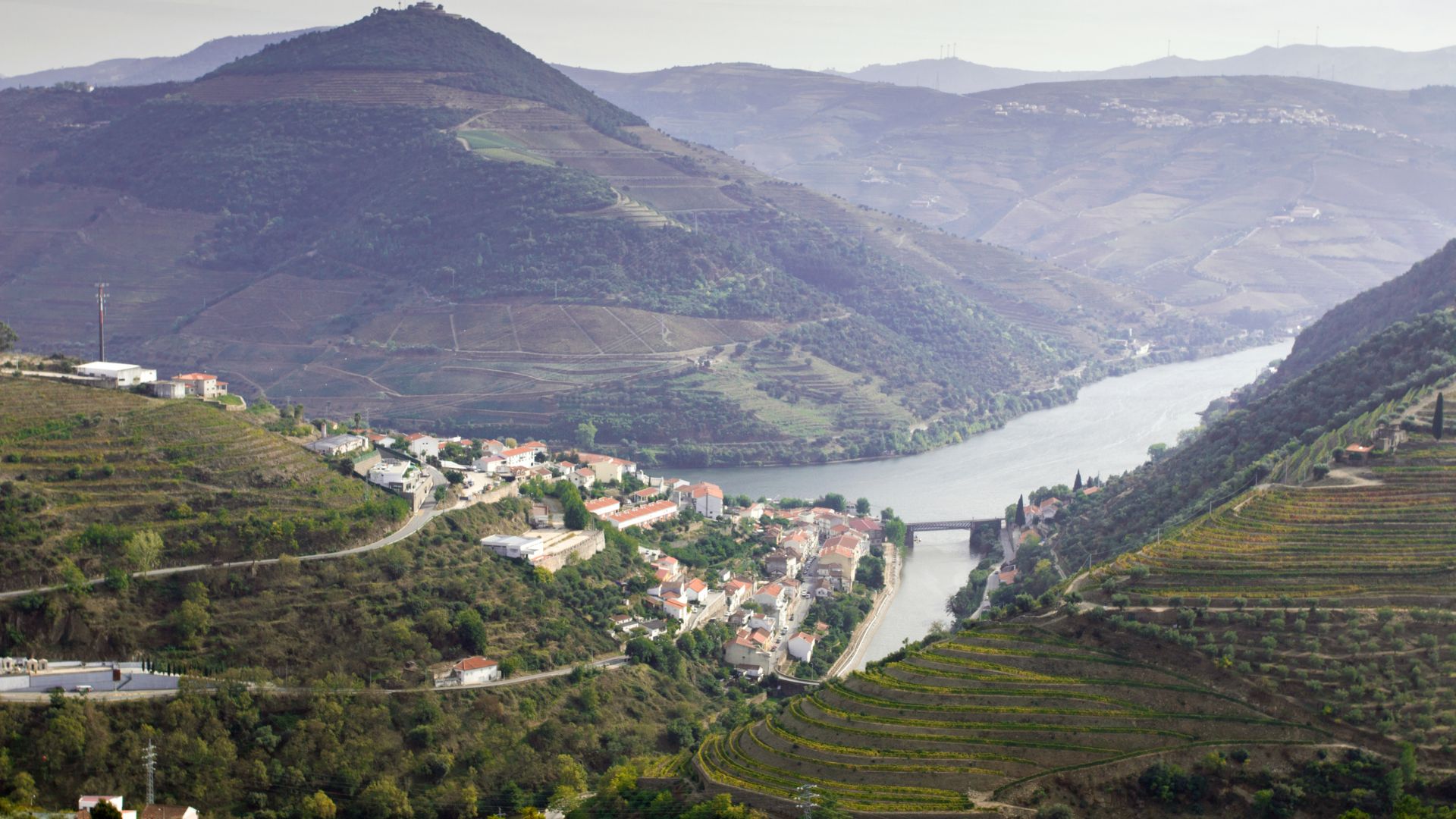 A scenic view of a village nestled in the terraced hills of the Douro Valley, with the Douro River winding through the landscape.