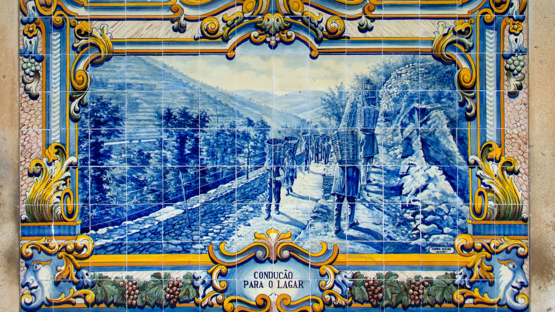 A blue and white azulejo tile panel at Pinhão Railway Station depicting a scene of figures walking along a path in a mountainous, vineyard-filled landscape.