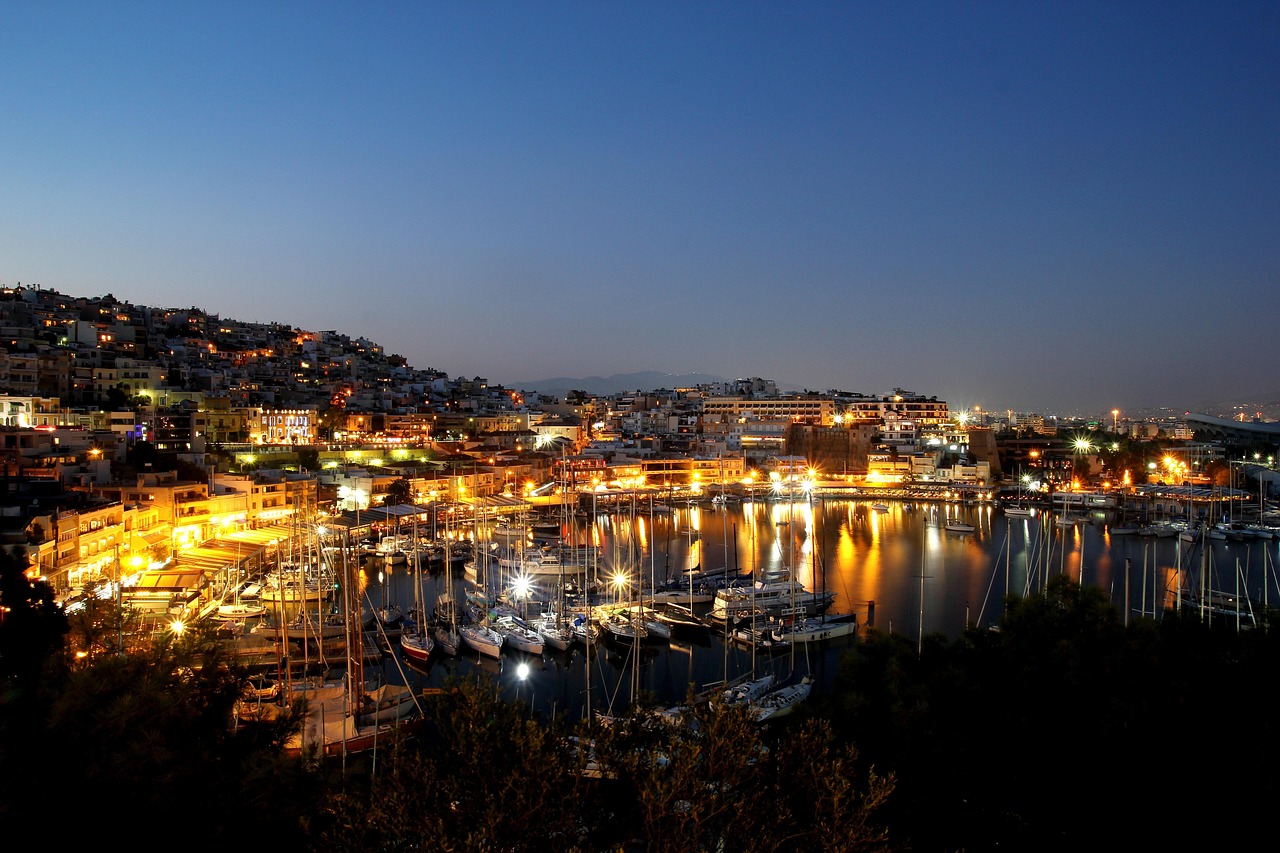 Night view of Piraeus, Greece with illuminated buildings and yachts docked in the harbor.
